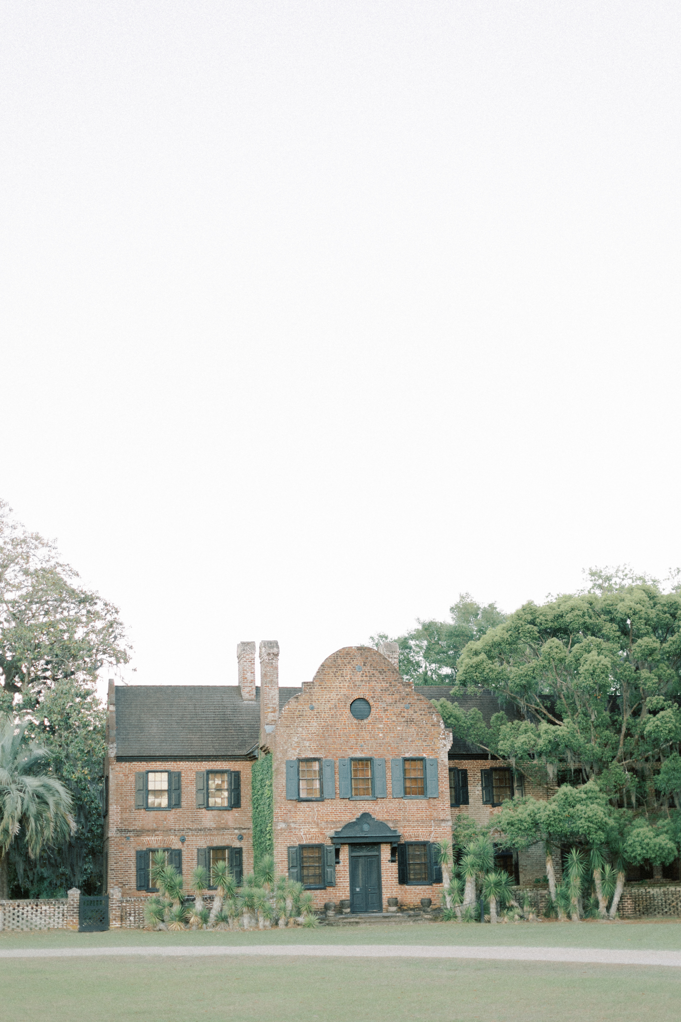 Brick mansion with a curved Dutch gable and round window above a wide lawn — a historic Charleston wedding venue, middleton place