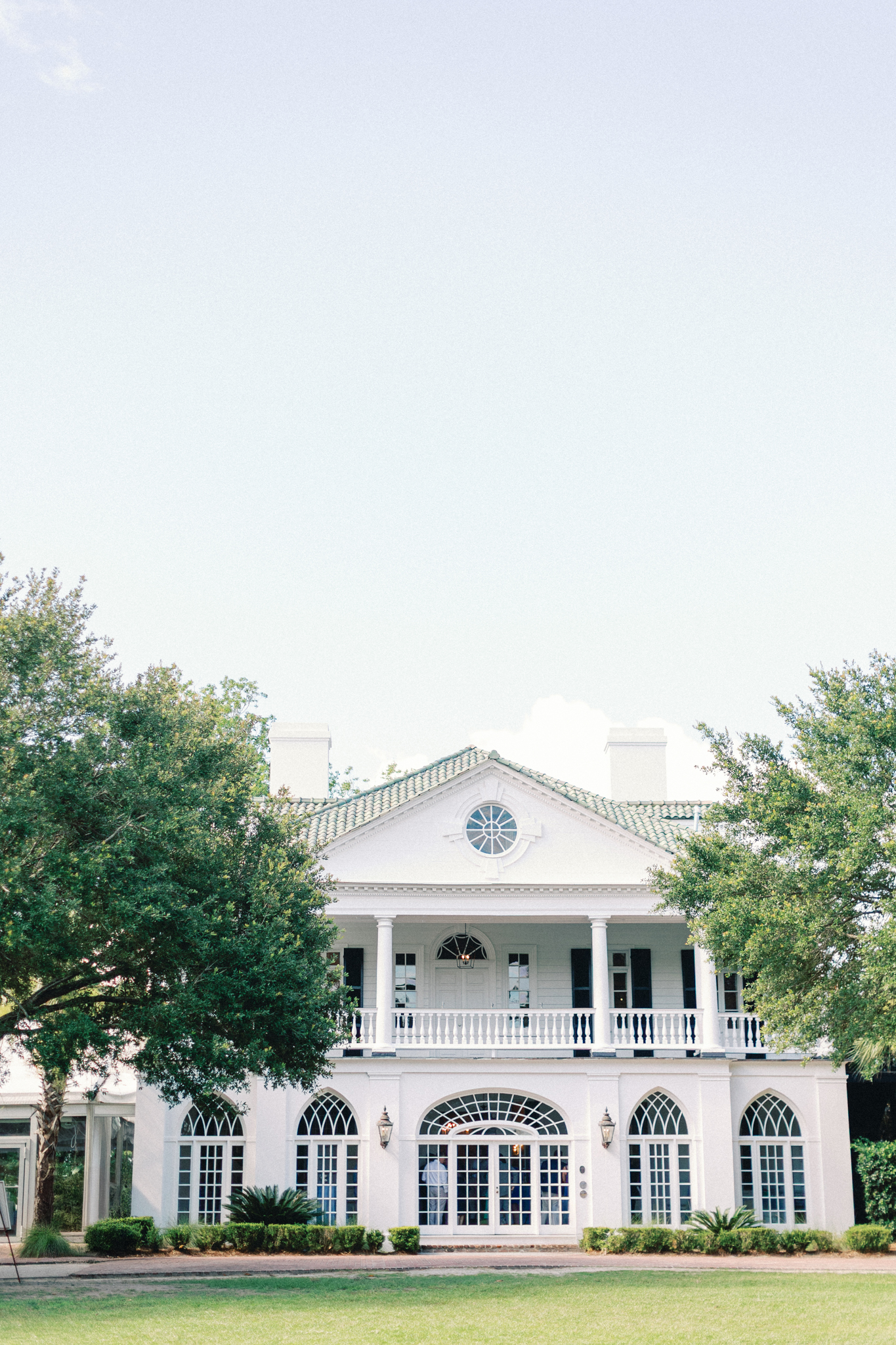 White mansion with a green tile roof, double portico and arched loggia windows framed by live oaks — a Charleston wedding venue lowndes grove