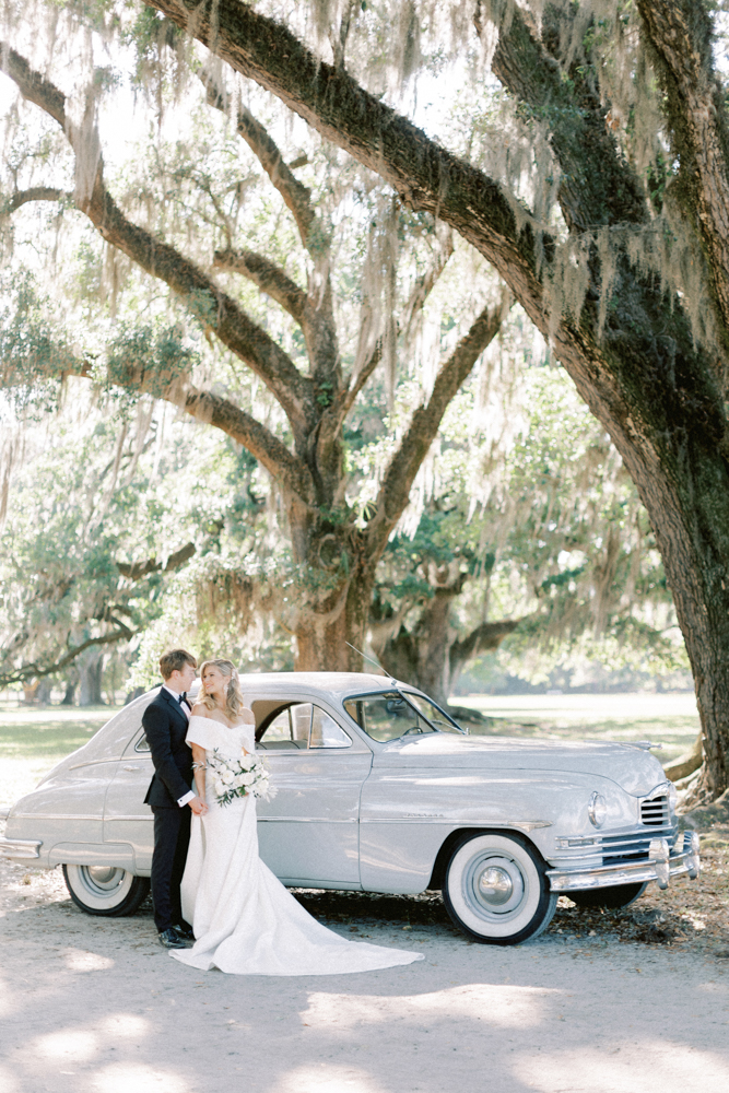 bride and groom in front of blue getaway car