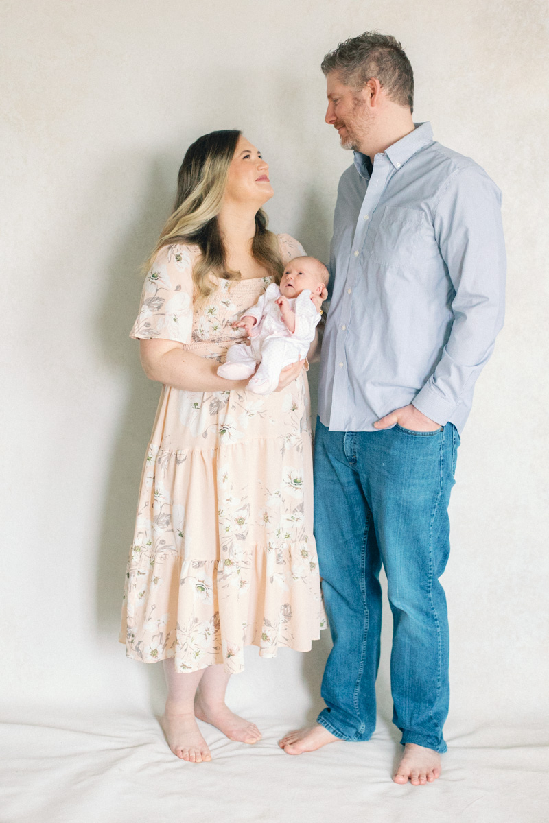 parents with newborn baby in front of fine art backdrop