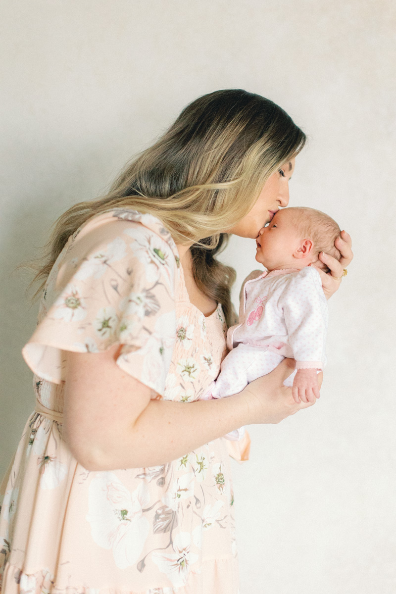 mom with newborn baby in front of fine art backdrop kissing head