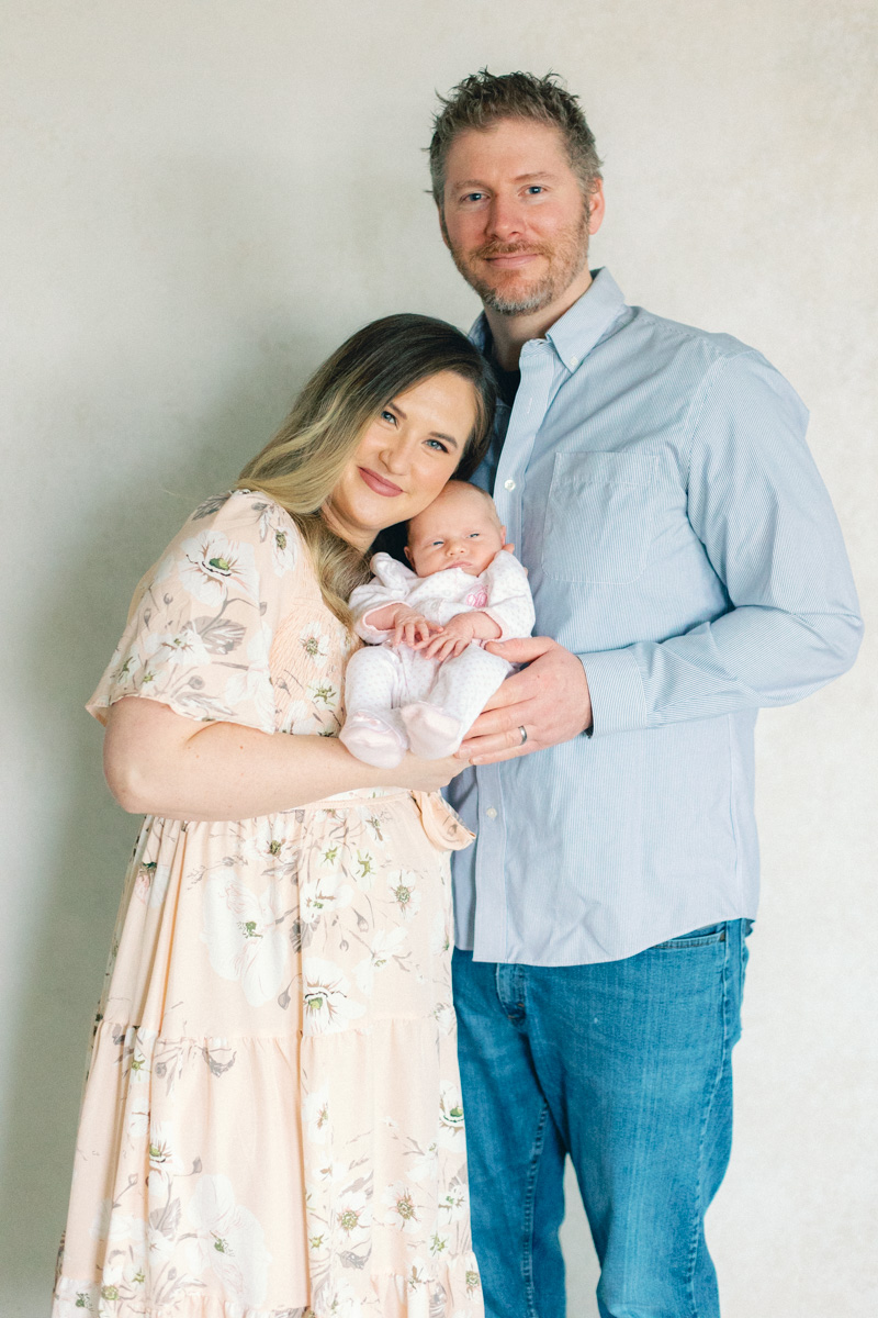 mom and dad with newborn baby in front of fine art backdrop