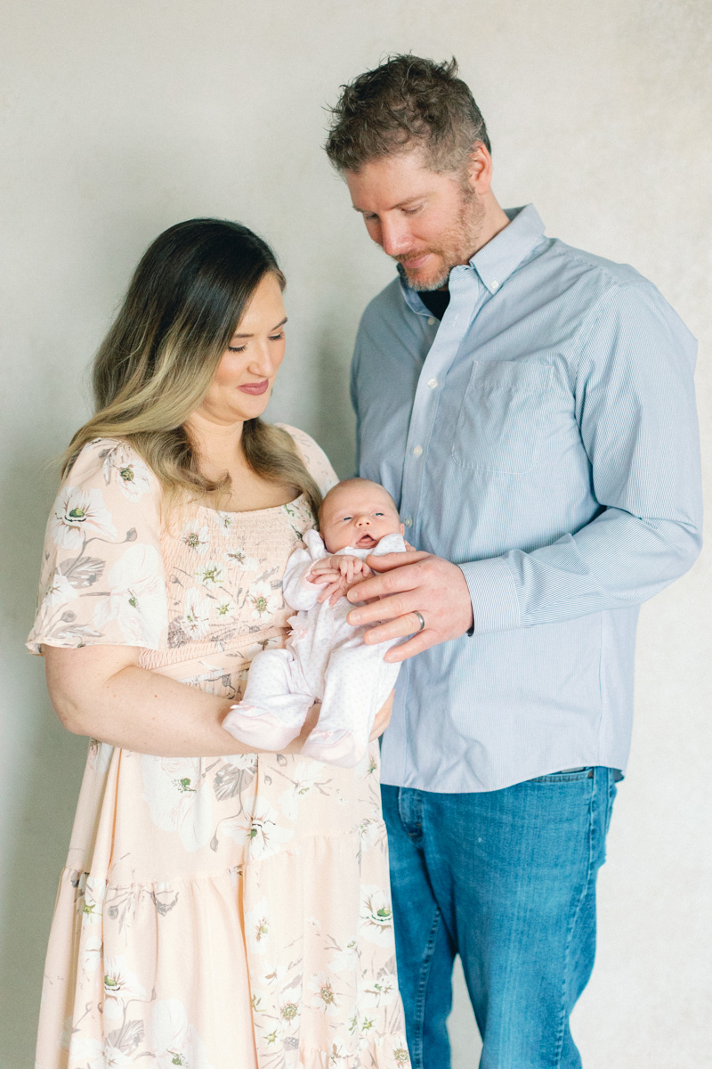 mom and dad with newborn baby in front of fine art backdrop