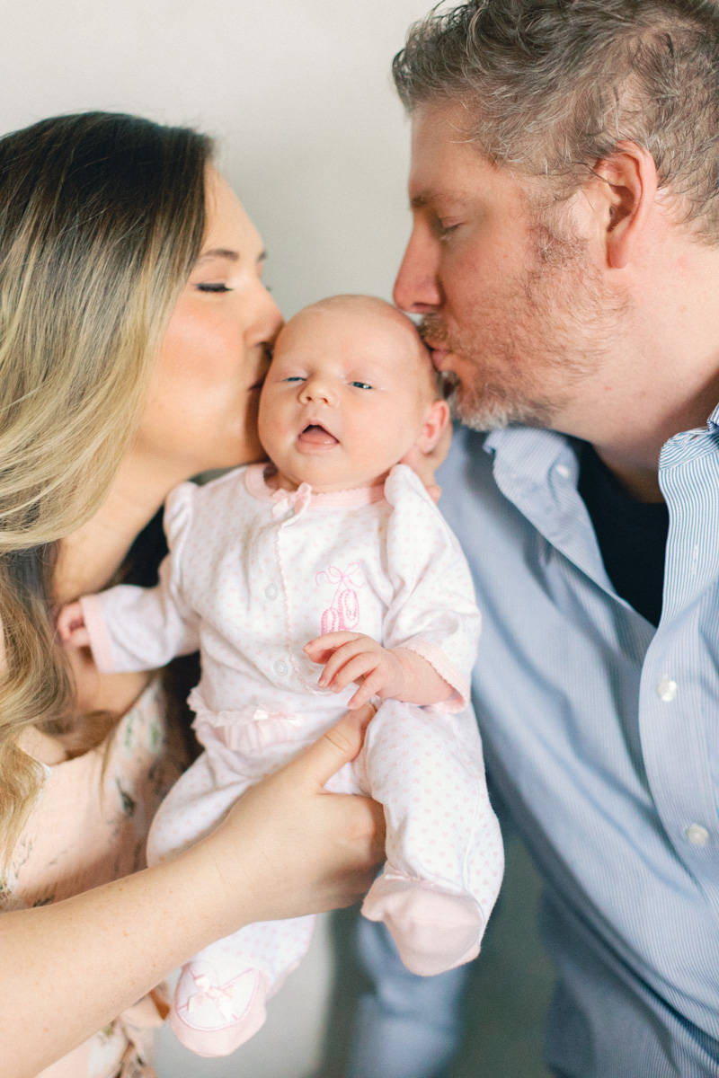 mom and dad kissing newborn baby close up