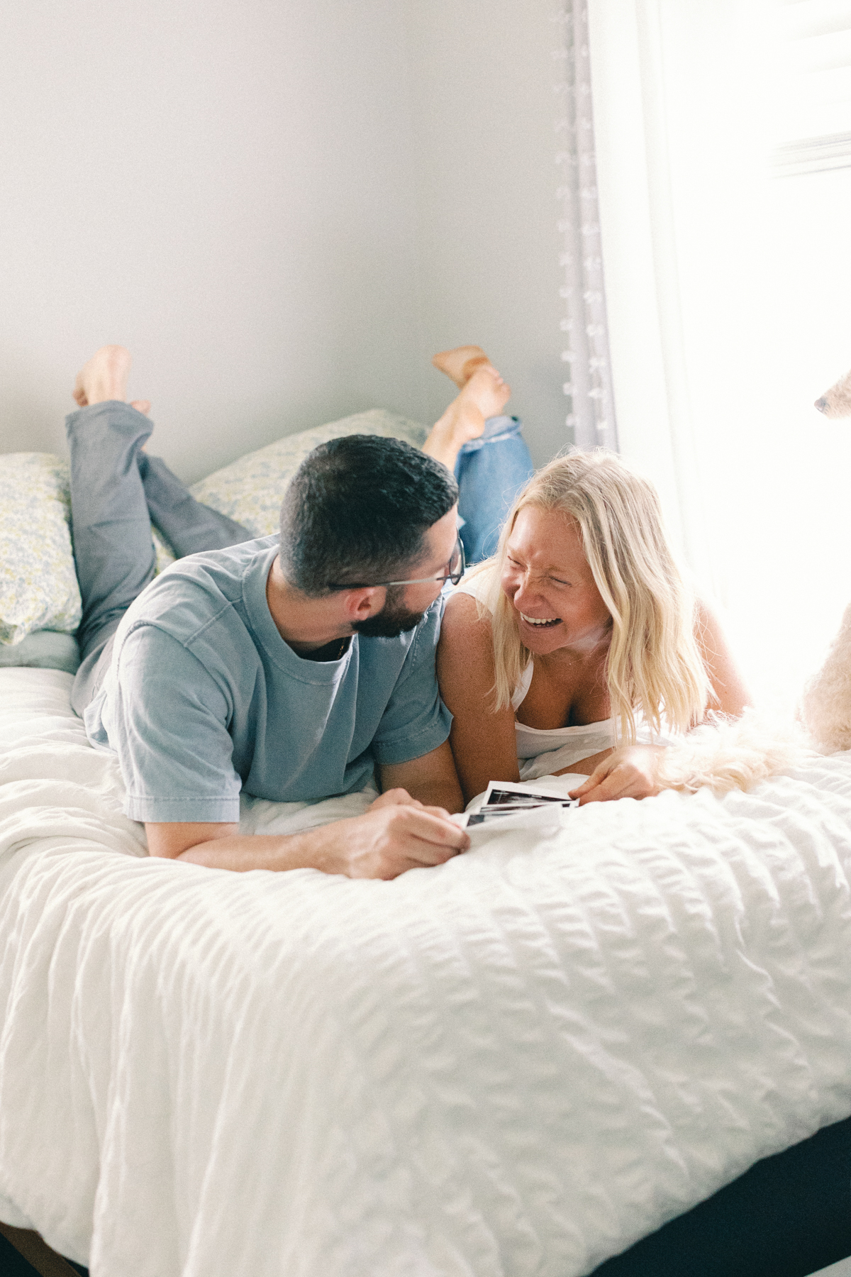couple laying in bed looking at ultrasound picture laughing