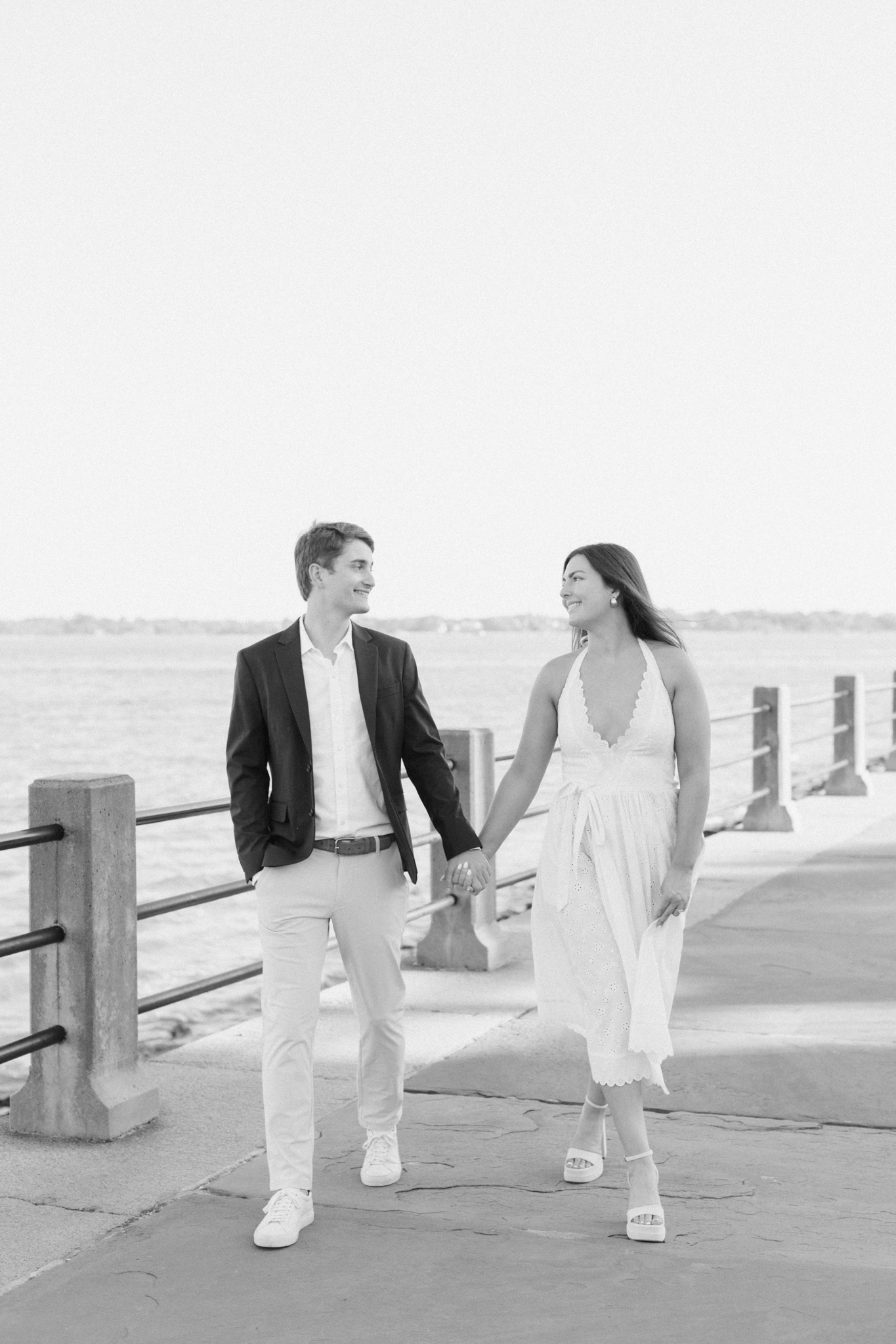 Black and white photo of a couple walking The Battery seawall by Charleston Harbor during their engagement photos