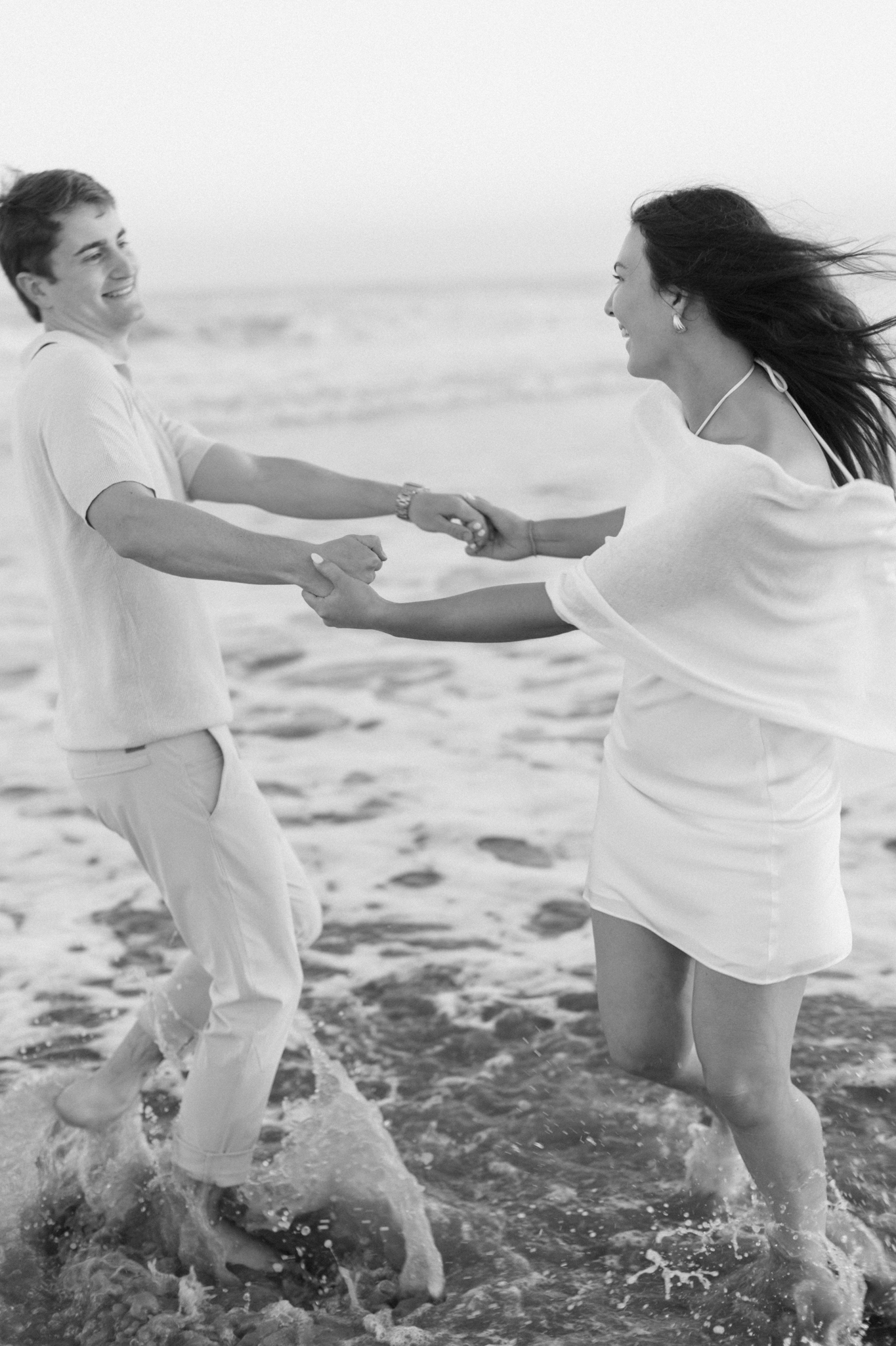 Black and white photo of a couple laughing and spinning in the surf during a beach engagement session near Charleston