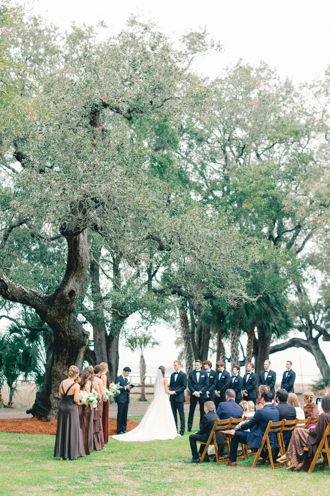 Bride and groom marry under live oaks by the water, bridesmaids in brown, at a waterfront Charleston waterfront wedding venue lowndes grove