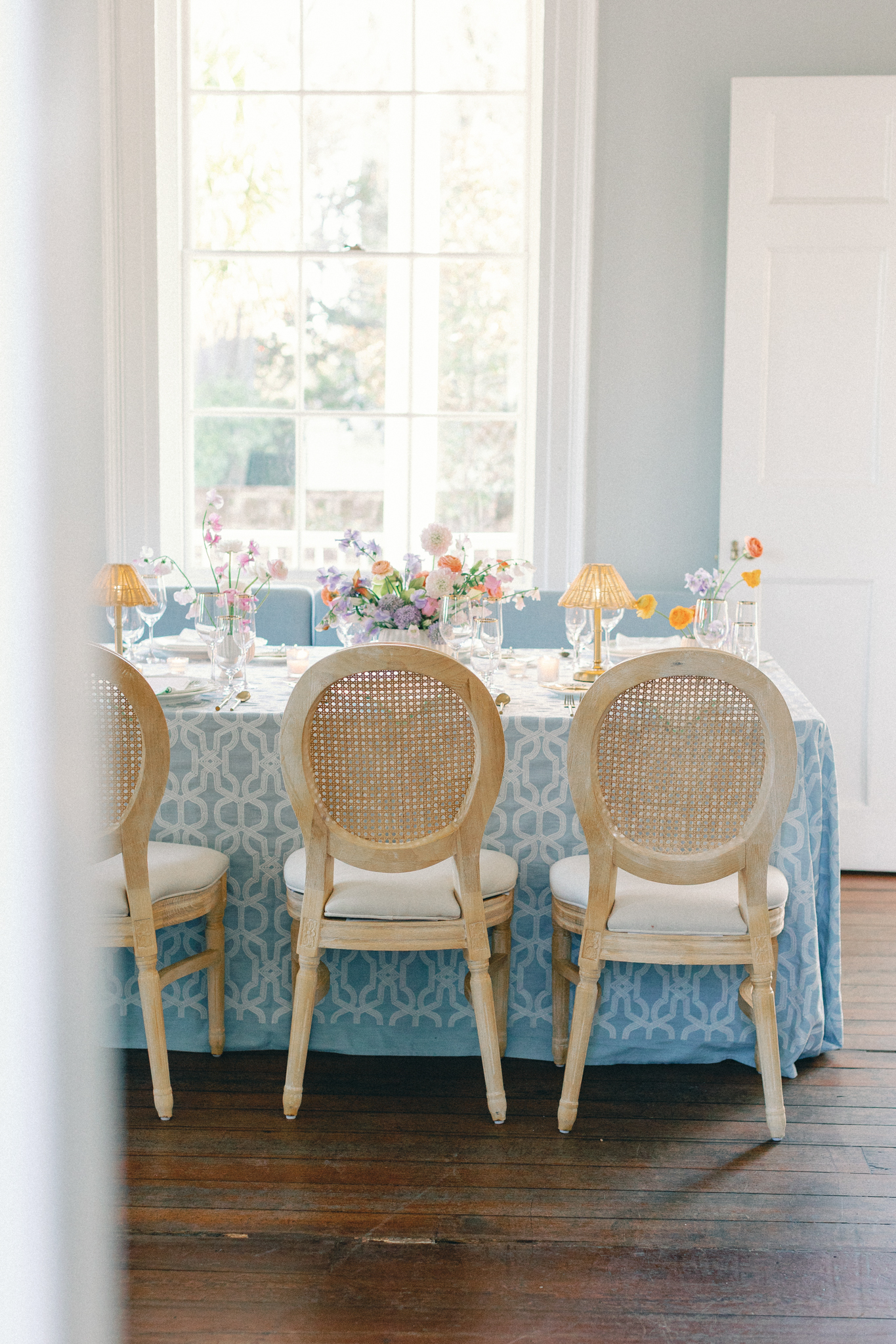 Historic room set with a blue cloth, cane chairs, and spring florals for an intimate Charleston wedding dinner, a planner's tablescape