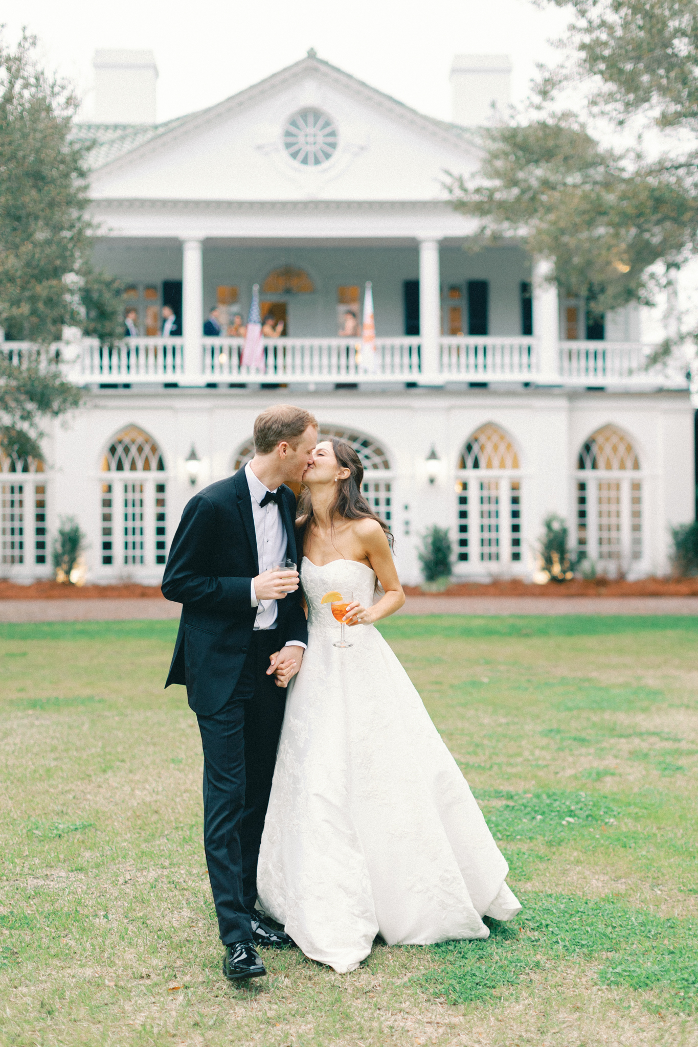 Bride and groom kissing on the lawn before the white columns of Lowndes Grove at a Charleston wedding