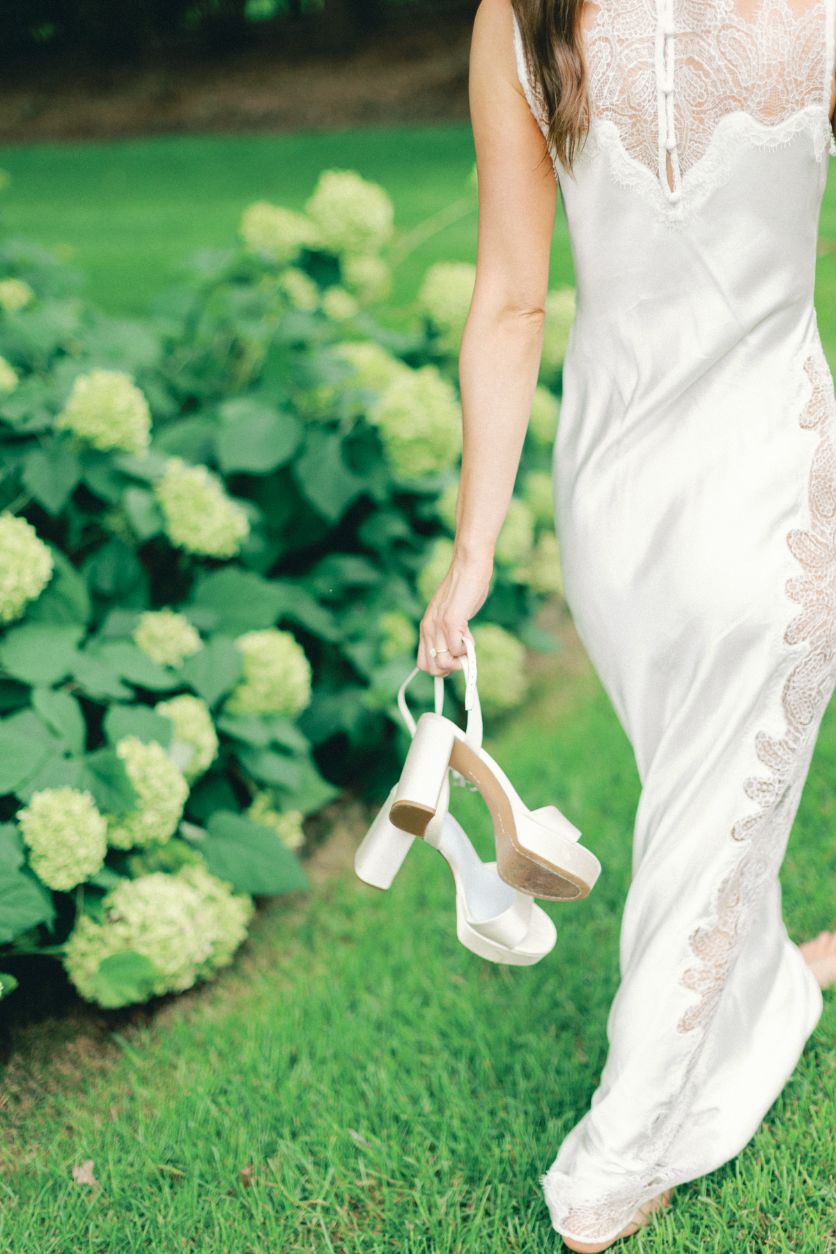Bride caring her shoes in front of flowers