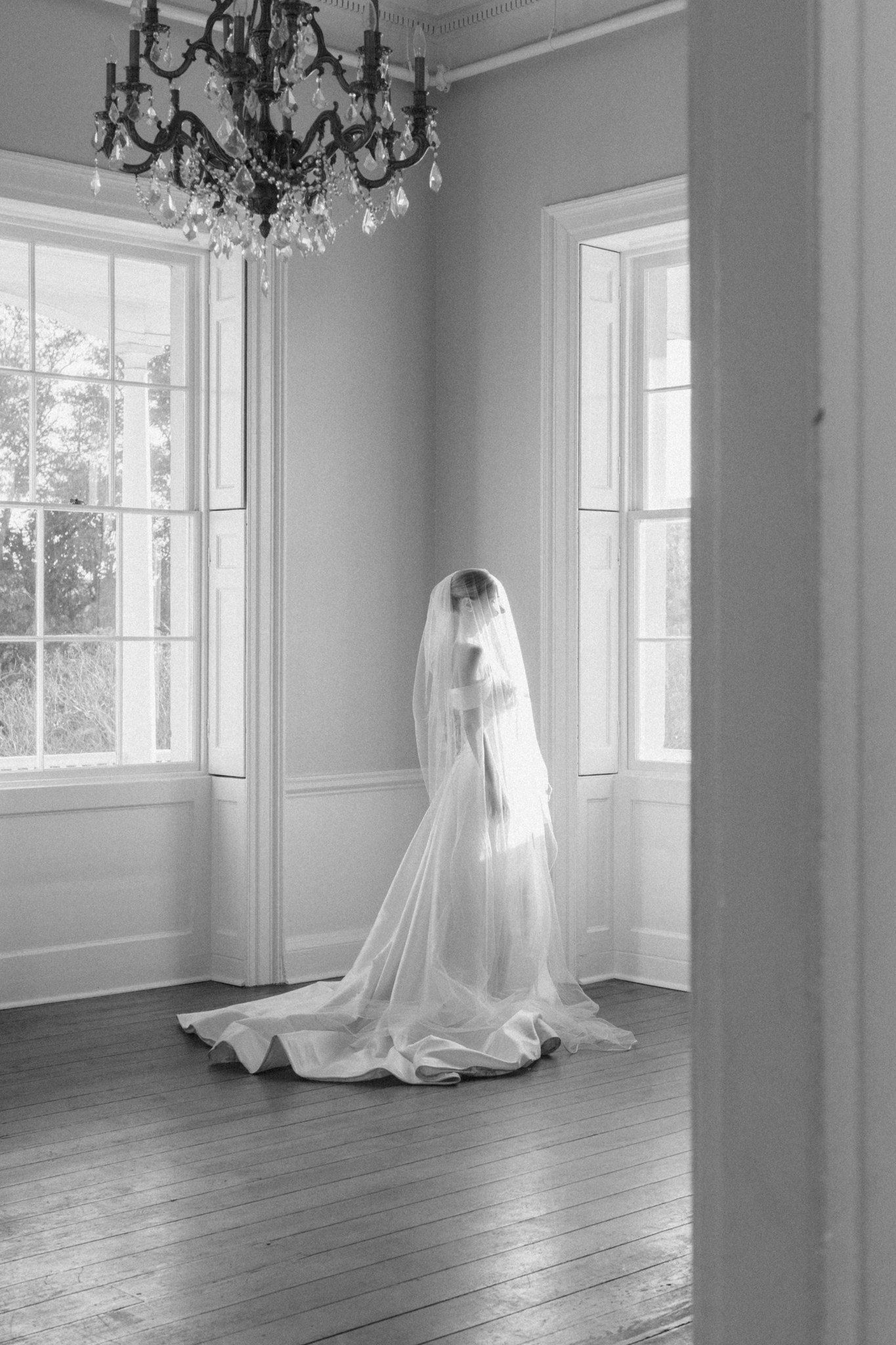 Black and white bridal portrait beneath a veil in a grand historic room with a chandelier, getting married in Charleston