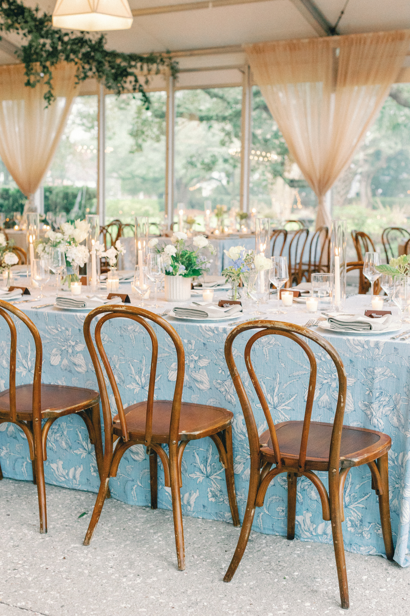 Tented reception with blue floral linens, bentwood chairs, and candlelight at a Charleston wedding