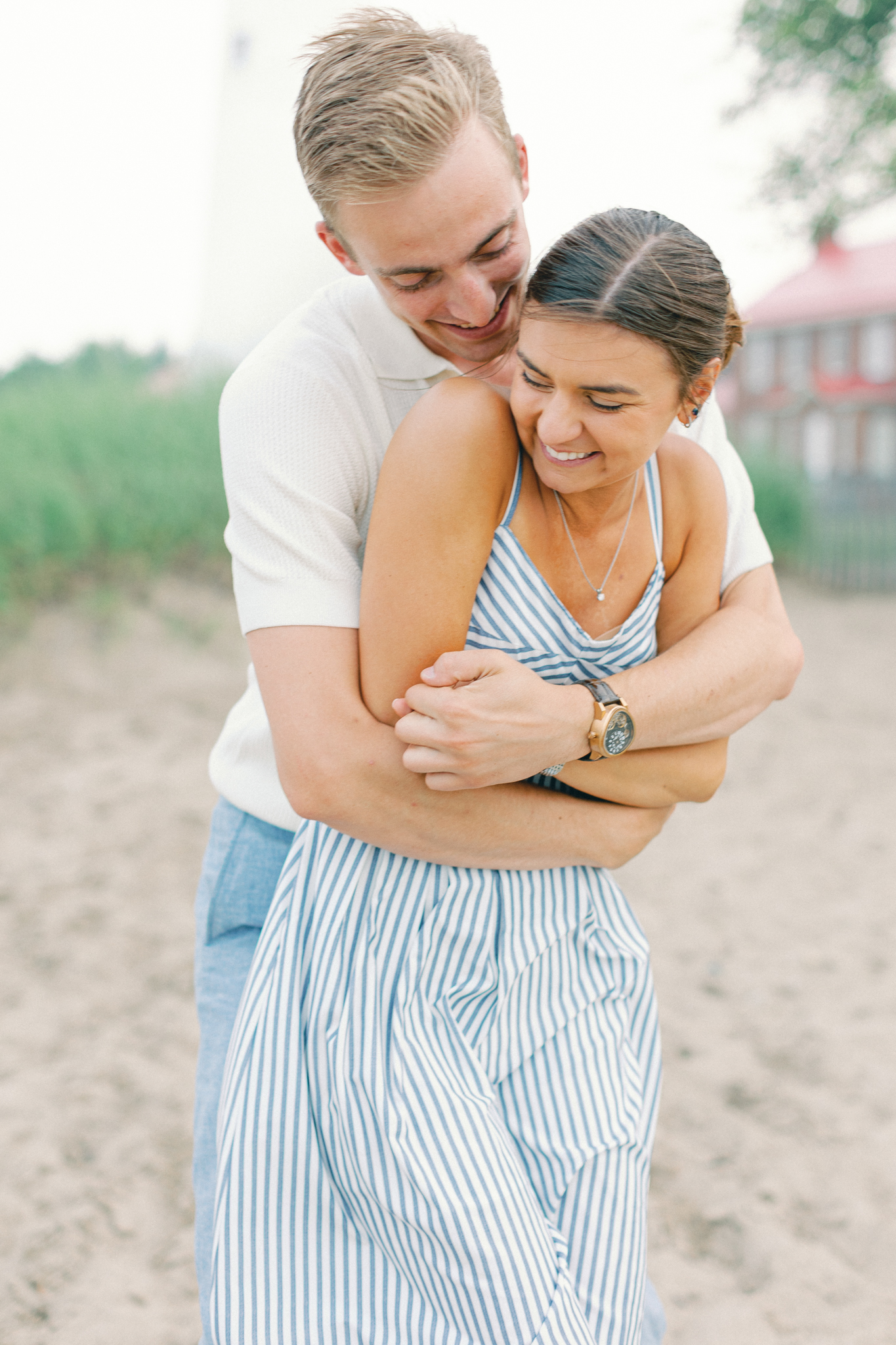 Caleb hugs Emma from behind near the Fort Gratiot Lighthouse during their Port Huron, Michigan engagement session.
