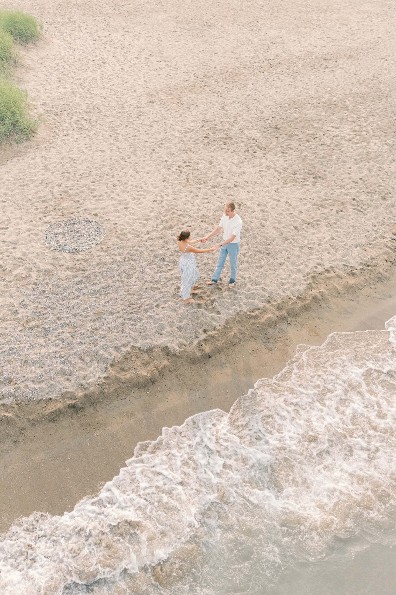 Aerial view of Emma and Caleb holding hands on the beach near the shoreline in Port Huron, Michigan.
