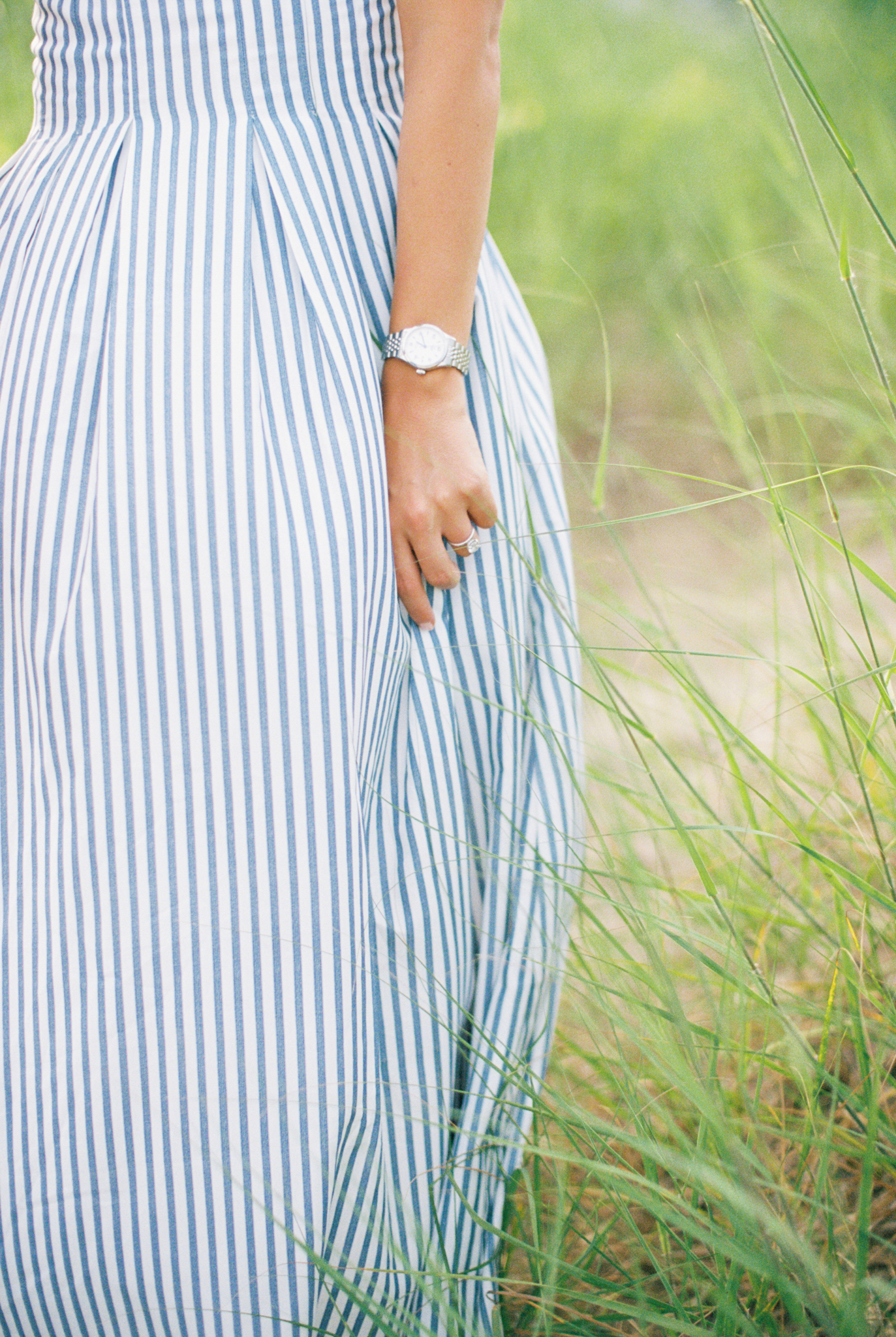 Close-up of Emma's striped dress and hand in the beach grass during her Port Huron, Michigan engagement session.