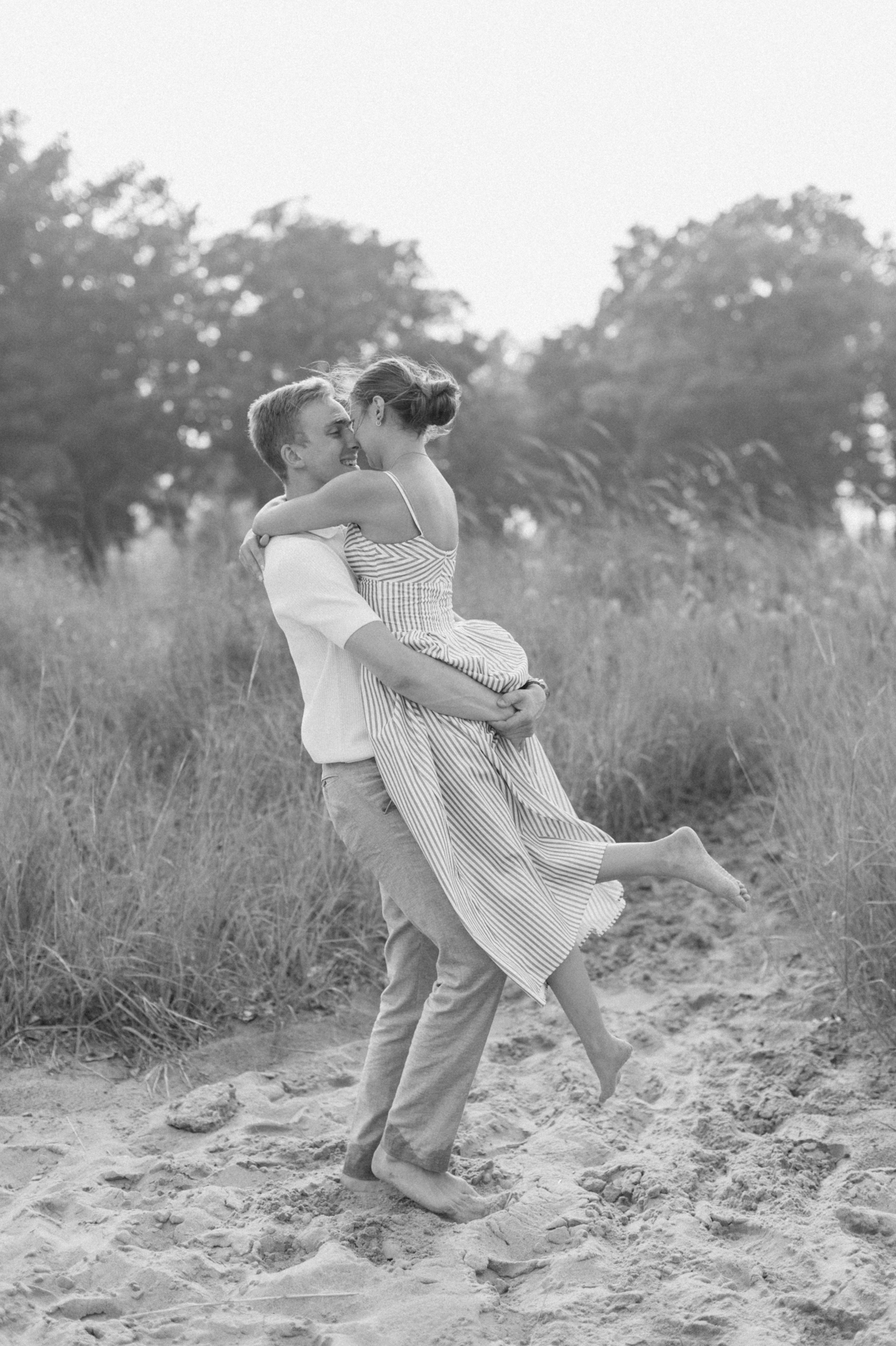 Black and white photo of Caleb lifting Emma as they embrace on the beach in Port Huron, Michigan.