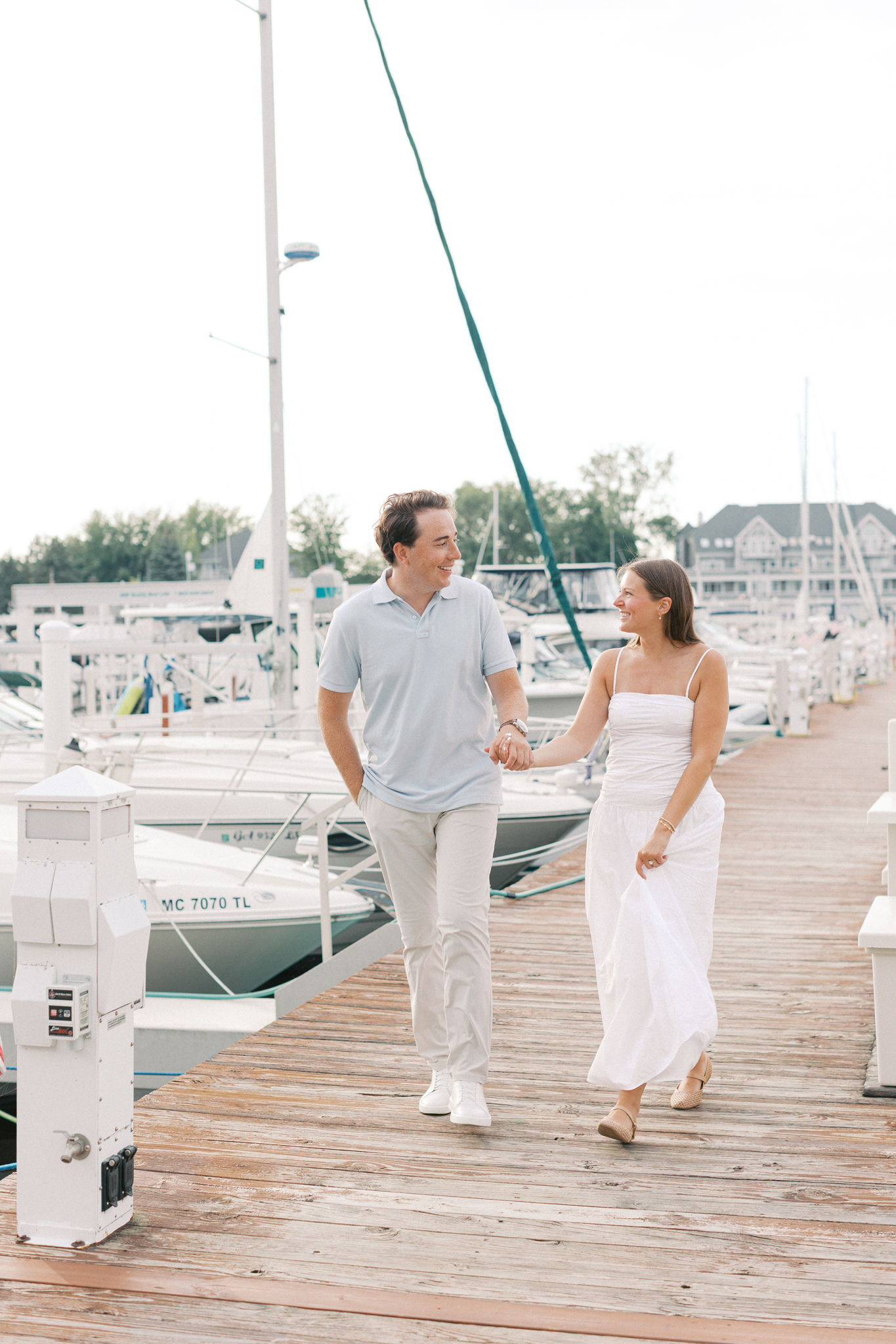 Lauren and Jason walking down a wooden marina dock lined with sailboats