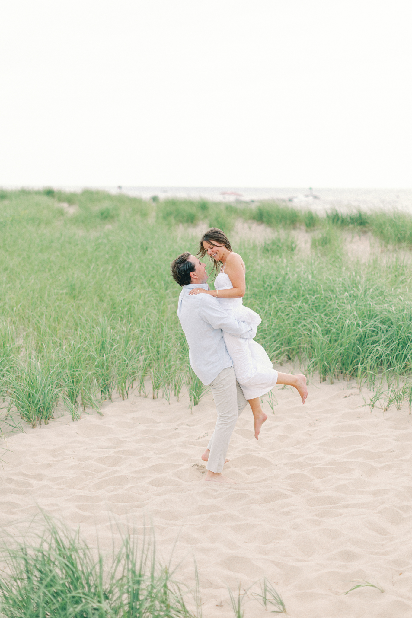 Jason lifting Lauren in the dune grass during their Lake Michigan engagement photos
