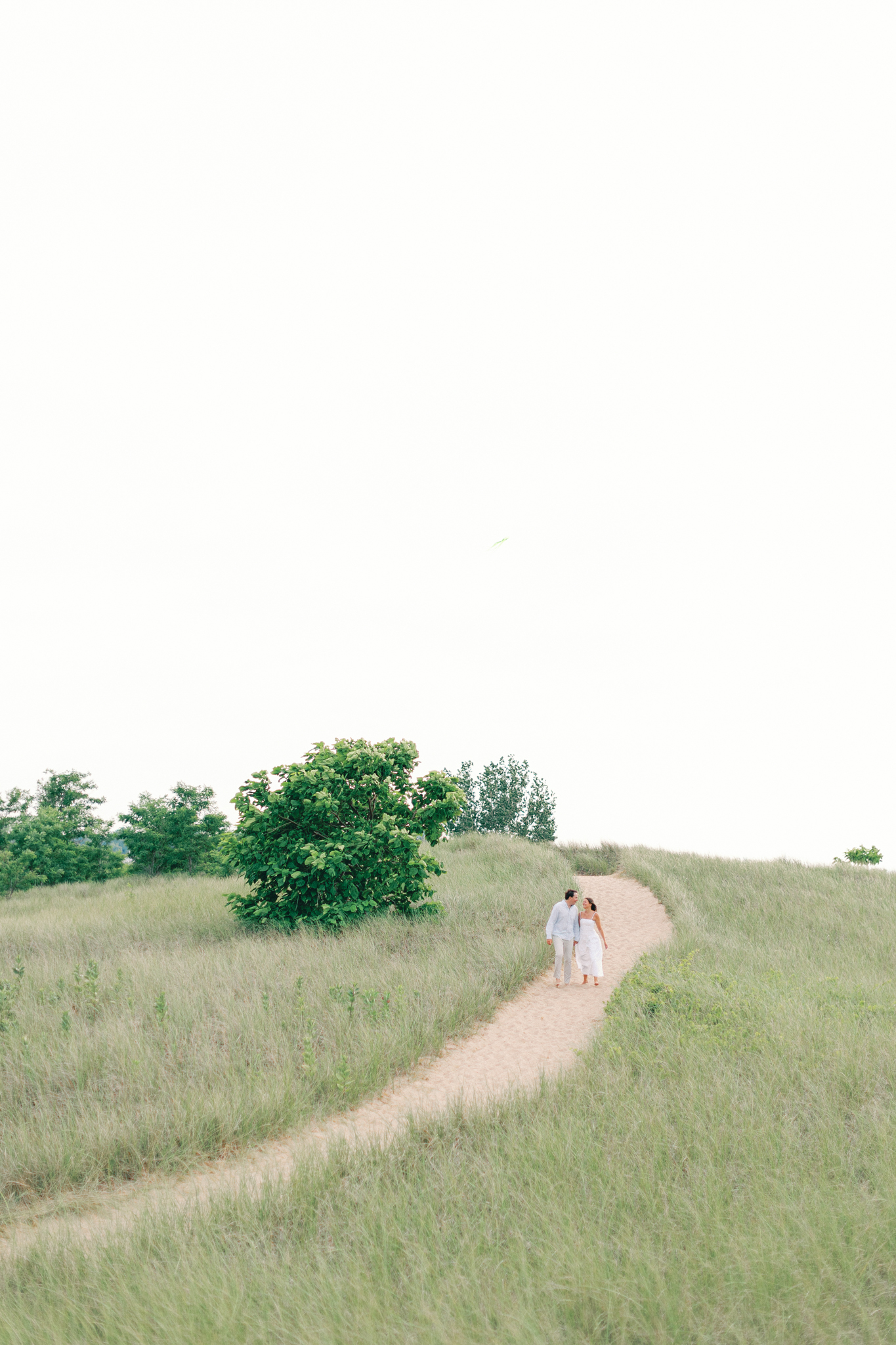 Wide view of Lauren and Jason walking up a winding grassy dune path in Michigan