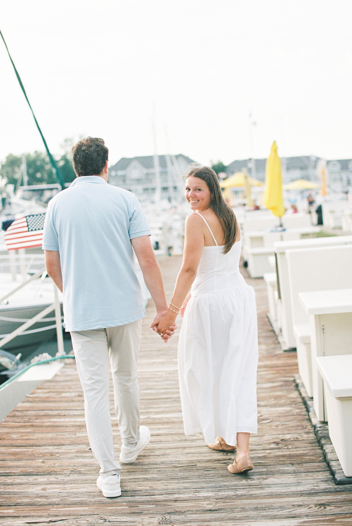 Lauren and Jason walking hand in hand down a marina dock among sailboats