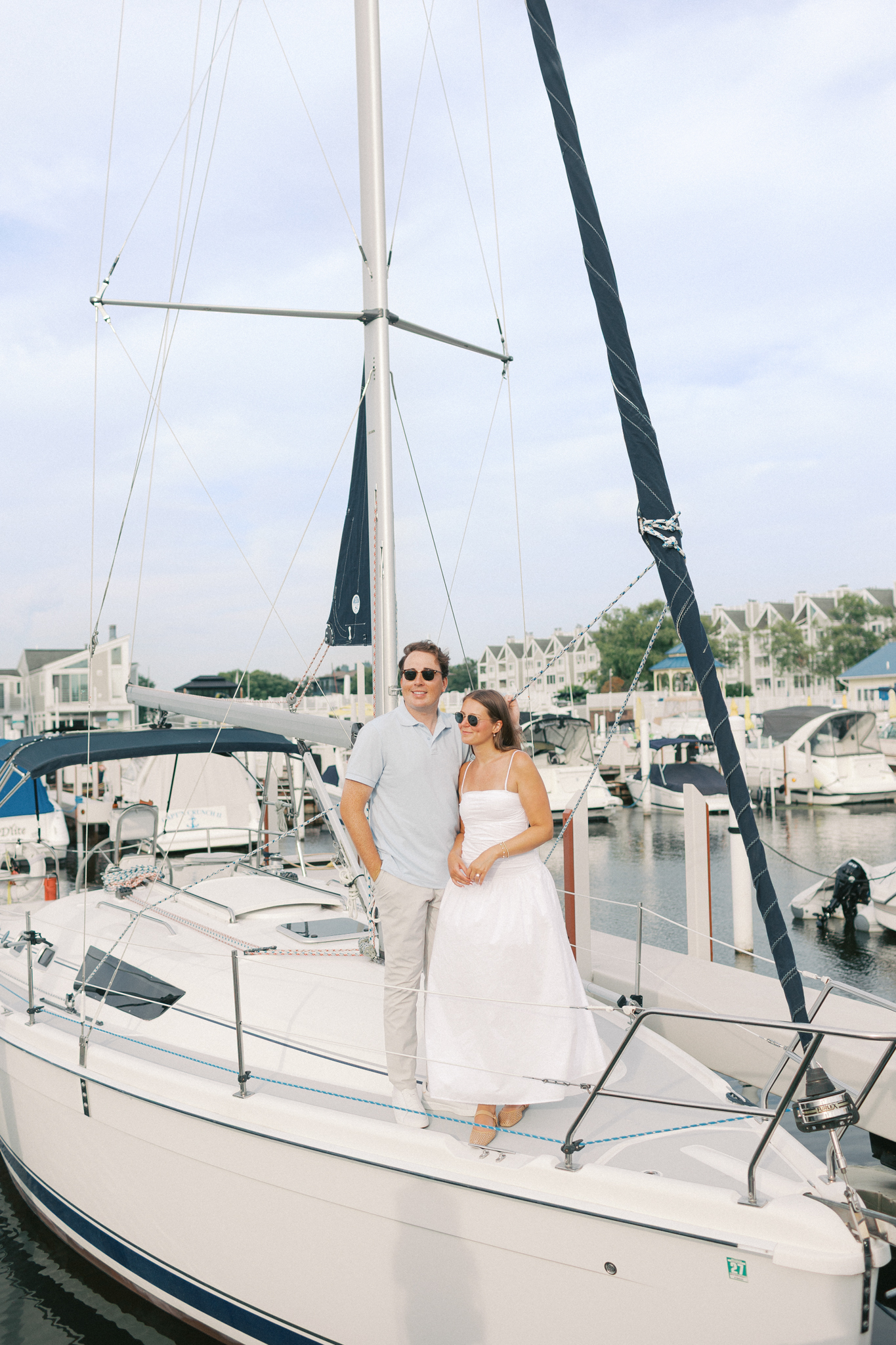 Lauren and Jason standing together on the deck of a docked sailboat in the harbor