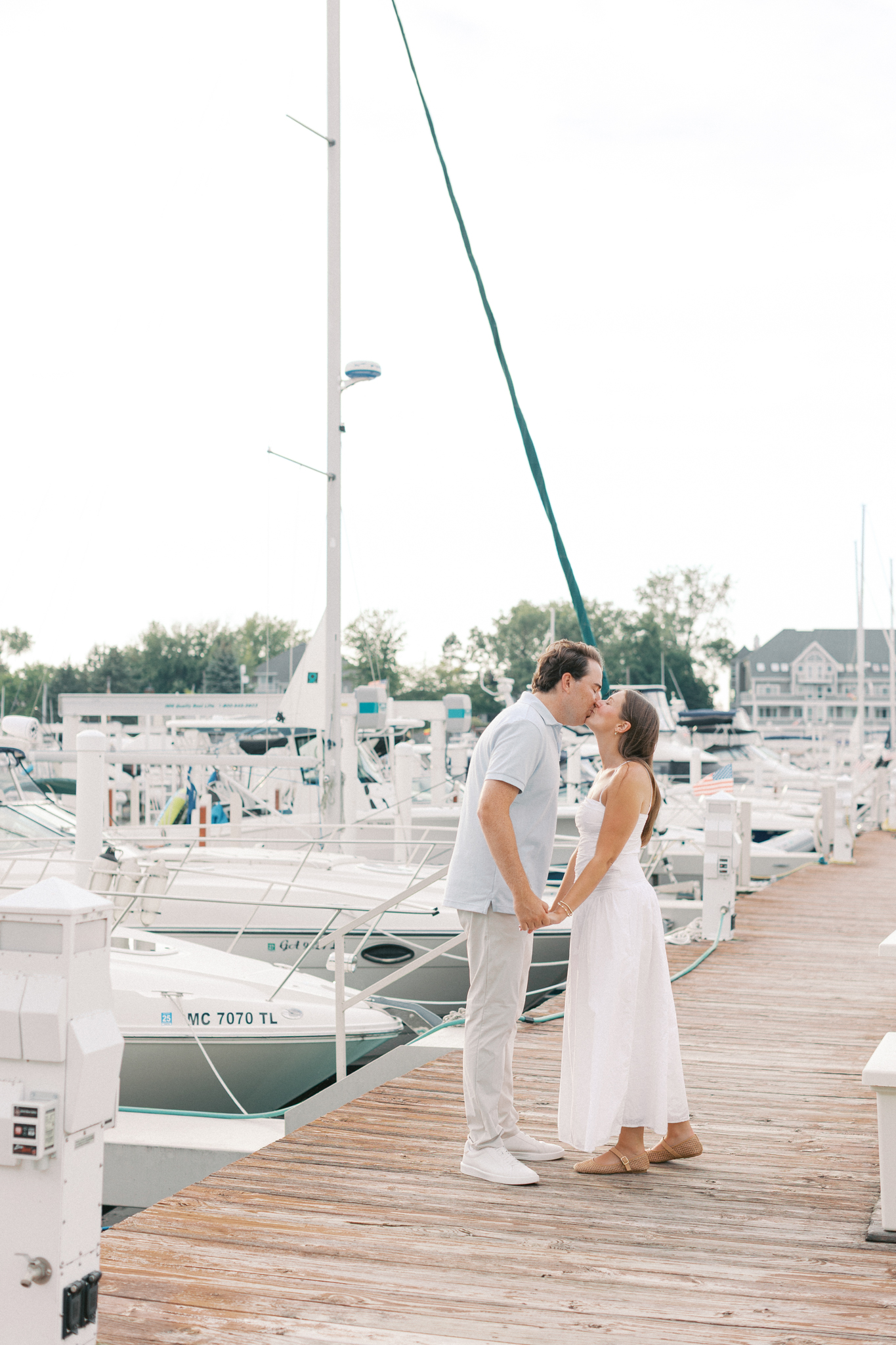 Lauren and Jason sharing a kiss on a wooden dock surrounded by sailboats