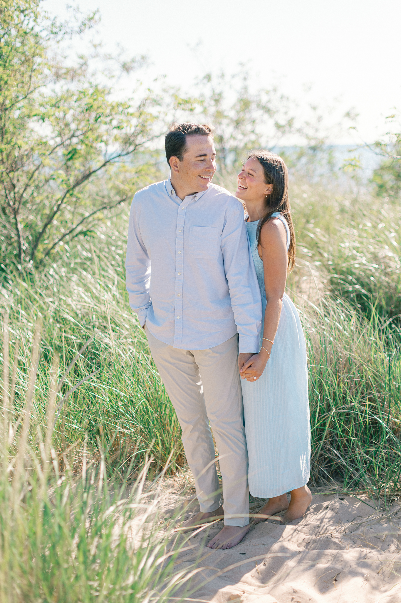 Lauren in a light blue dress standing with Jason in the dune grass during their South Haven, Michigan engagement session