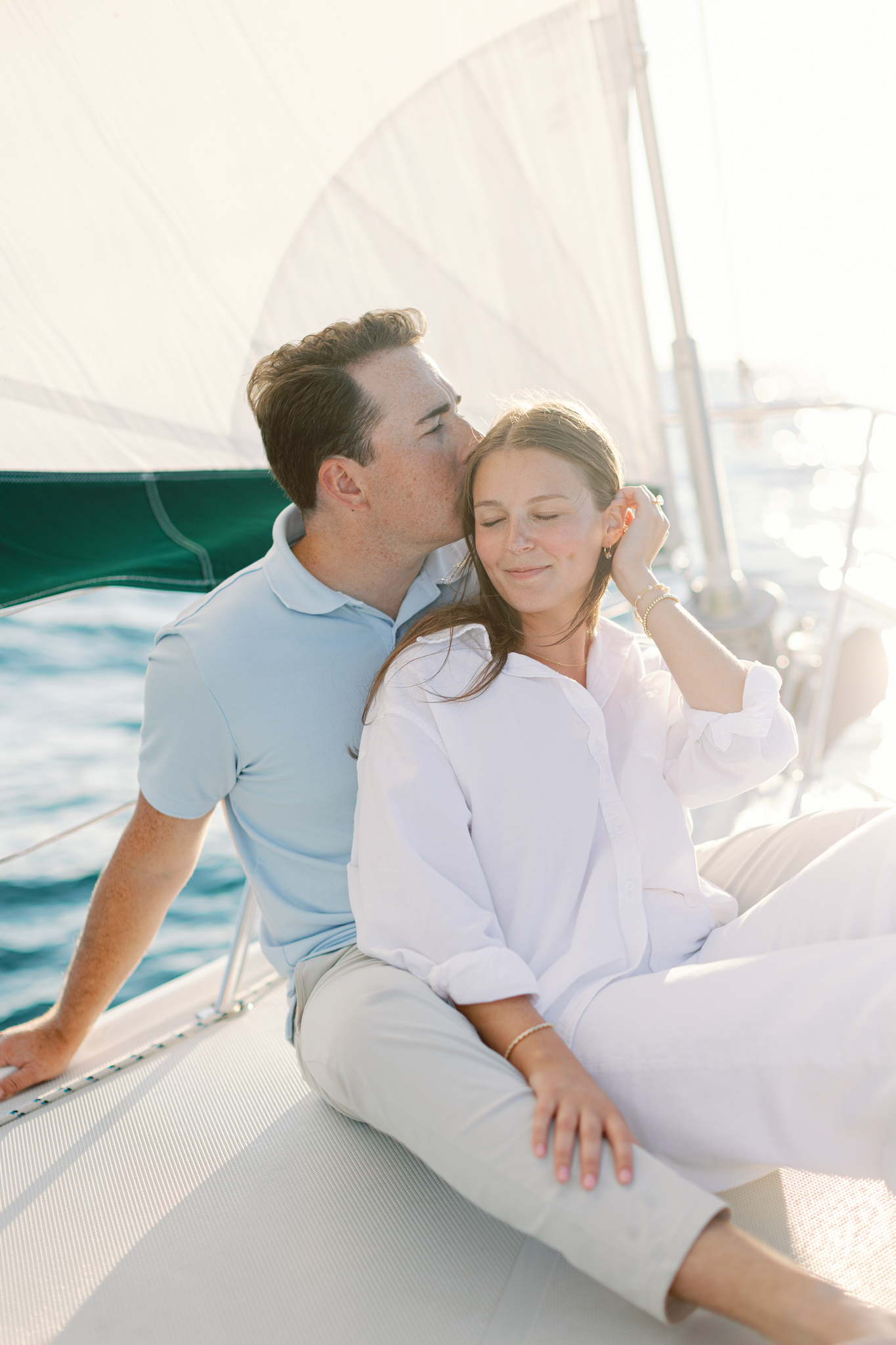 Jason kissing Lauren's forehead as they sit on the bow of a sailboat on Lake Michigan