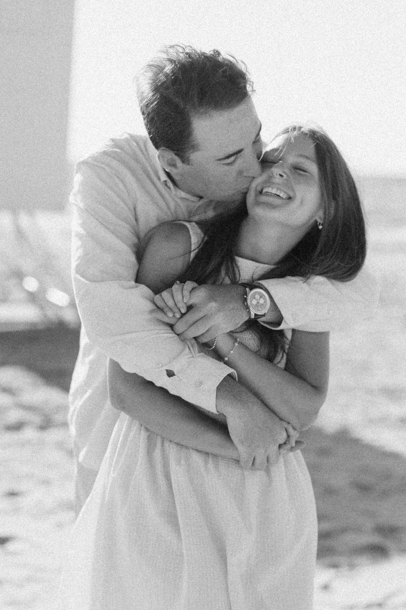Black and white photo of Jason hugging Lauren and kissing her cheek on the beach