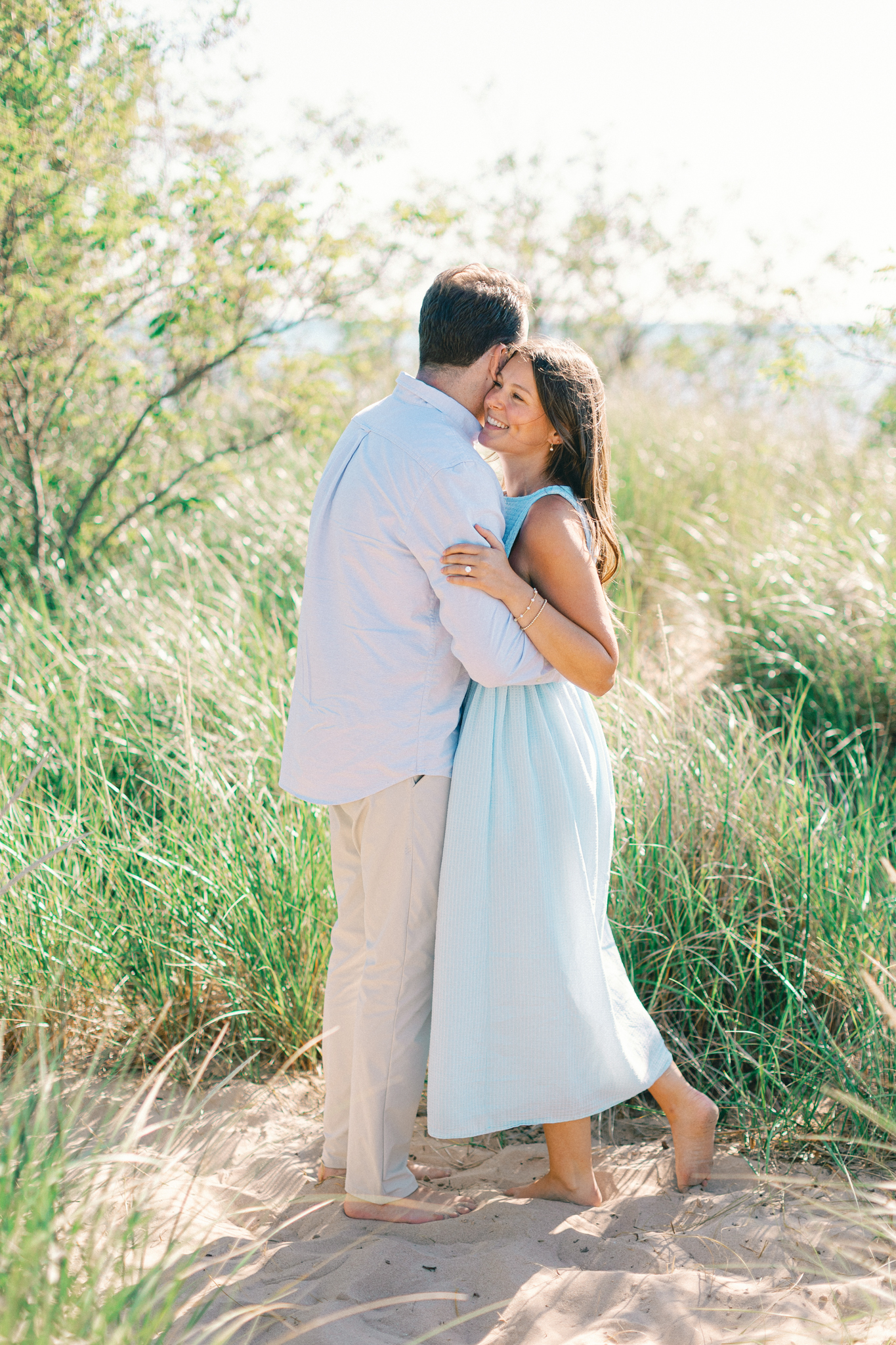 Lauren and Jason embracing among trees and dune grass in South Haven, Michigan