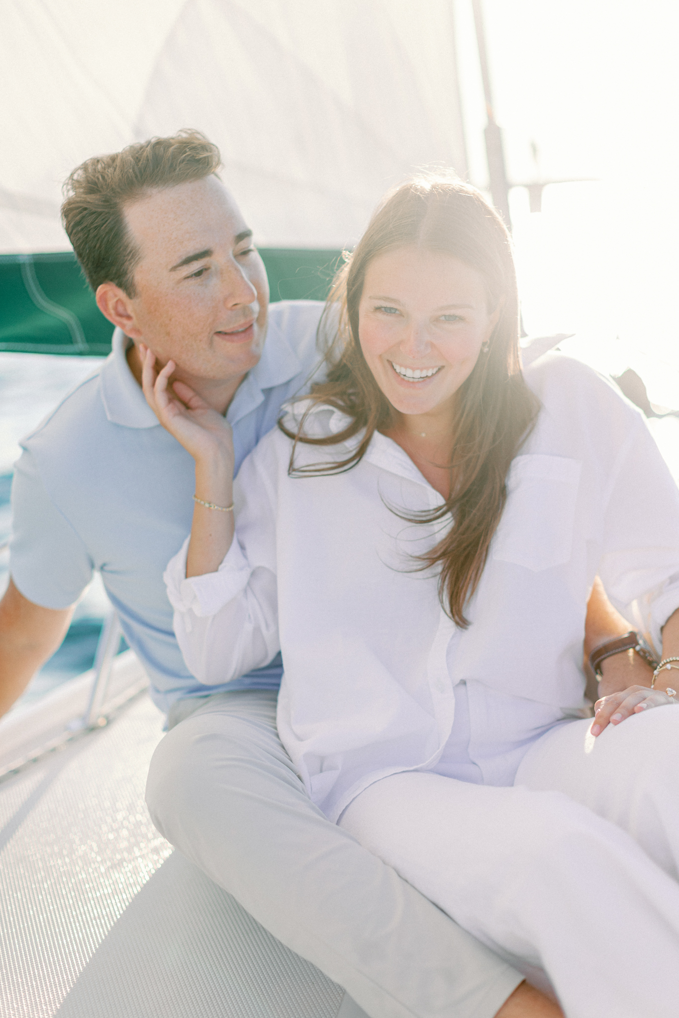 Lauren and Jason laughing together on the deck of a sailboat during their sailboat engagement session on Lake Michigan