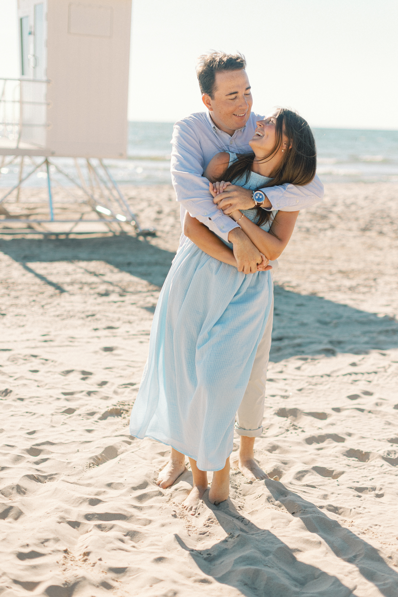 Jason hugging Lauren from behind near a lifeguard stand on the beach