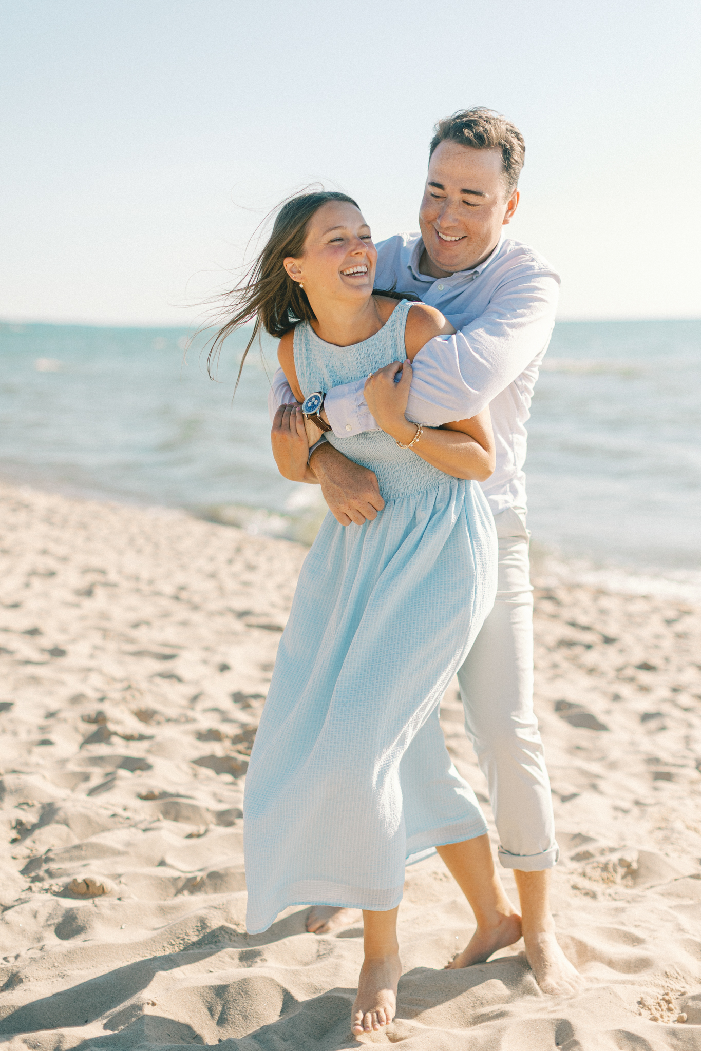 Lauren and Jason laughing in a hug along the Lake Michigan shoreline