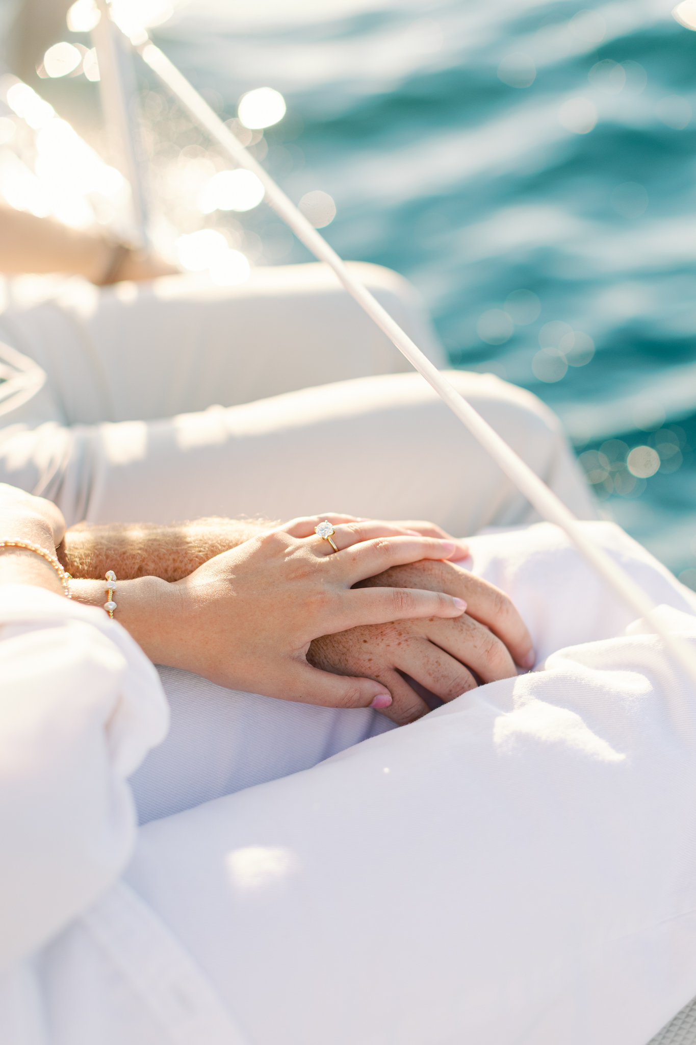 Detail of Lauren and Jason's hands resting together on a sailboat over blue water, from their sailboat engagement pictures