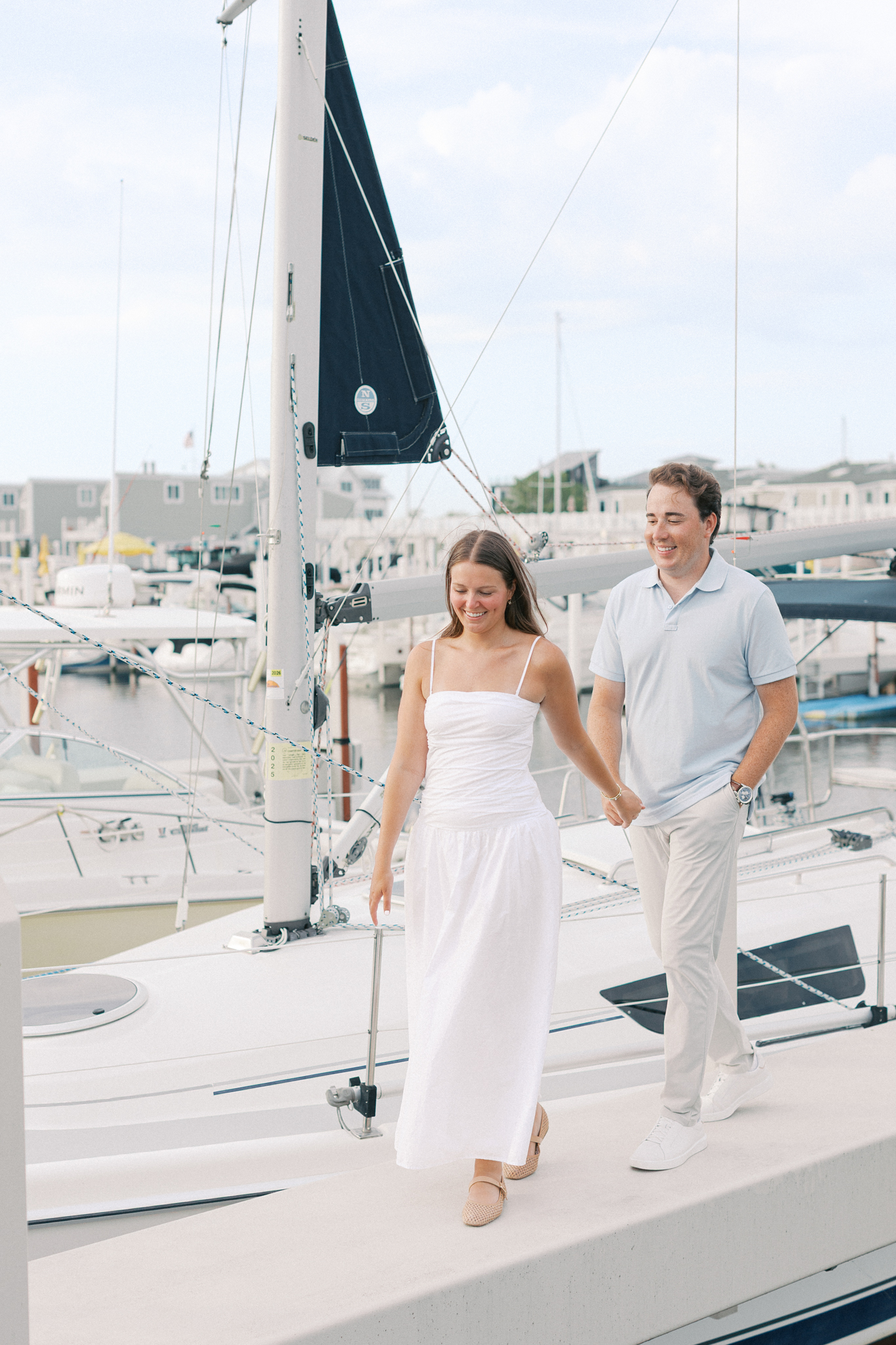 Lauren and Jason walking along the bow of a docked sailboat at the marina during their sailboat engagement session on Lake Michigan