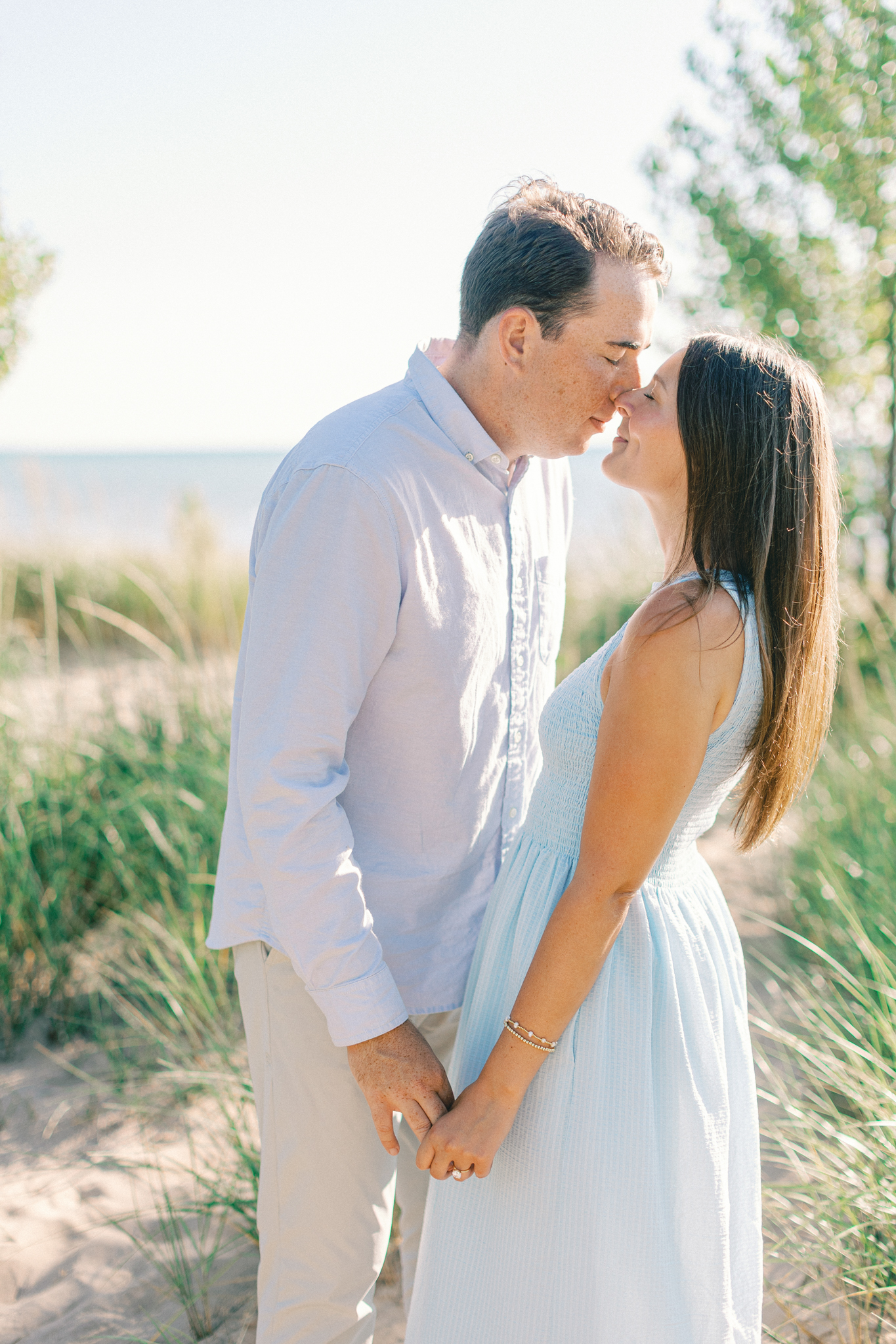 Lauren and Jason kissing on a sand dune with Lake Michigan in the background, from their Lake Michigan engagement photos