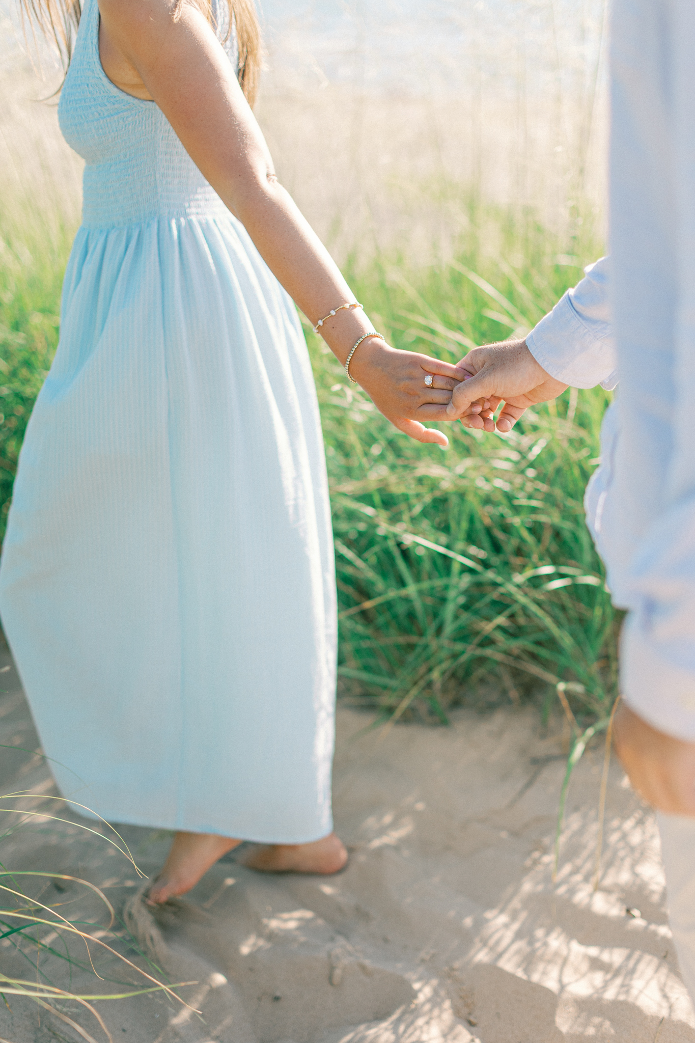 Detail of Lauren in a light blue dress holding Jason's hand in the beach grass