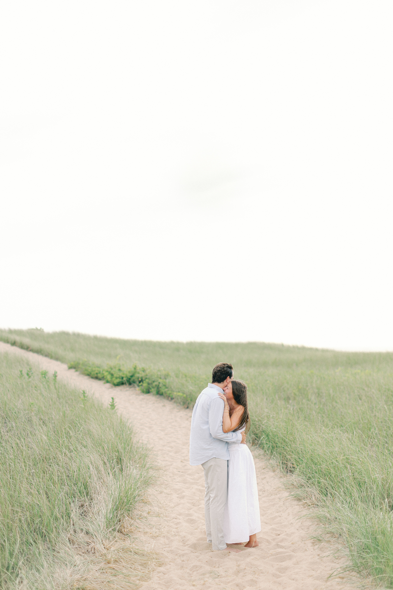 Lauren and Jason embracing on a long dune path under an open sky