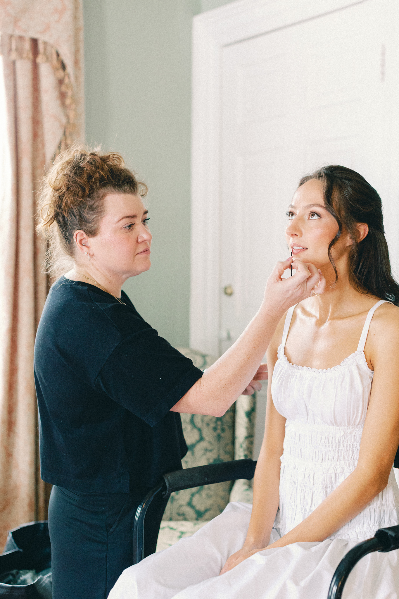 Makeup artist applies lipstick as the bride gets ready in a light-filled room ahead of her Charleston wedding