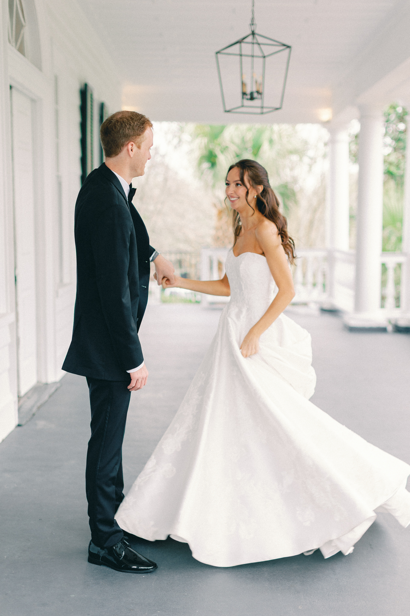 Bride twirls in her gown holding hands with the groom on a columned porch — a Charleston wedding first look