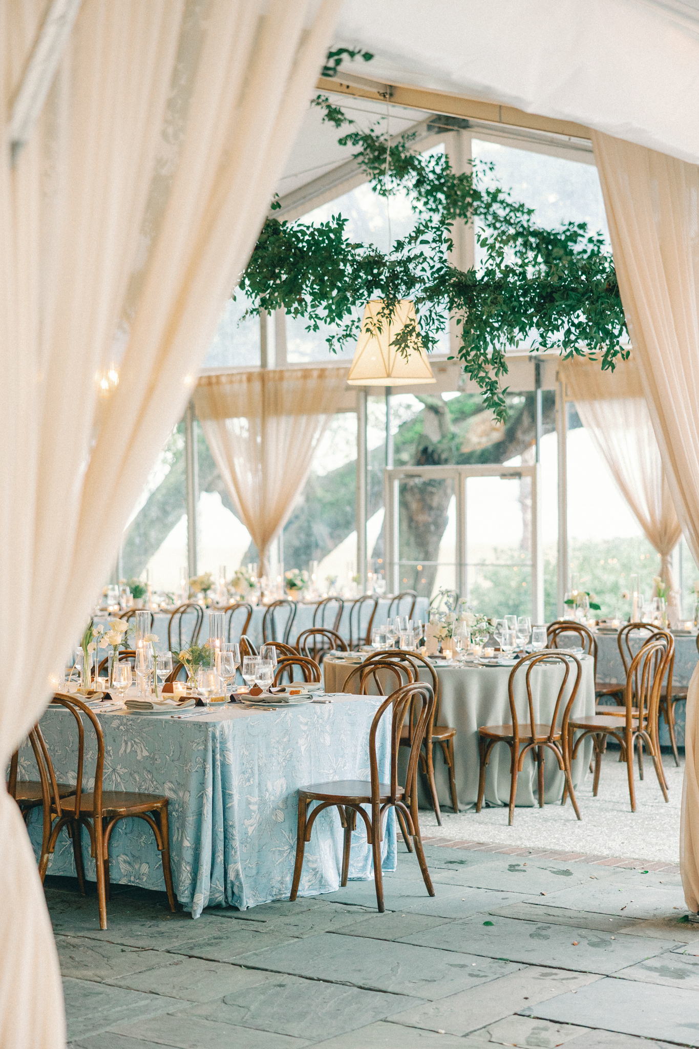 Tented reception with greenery overhead, blue floral linens and bentwood chairs at a Charleston wedding venue