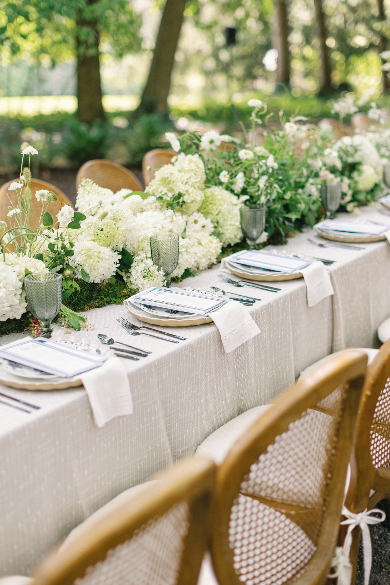 linen-draped long table with white hydrangea floral runner and rattan chairs at Greencrest Manor outdoor wedding reception