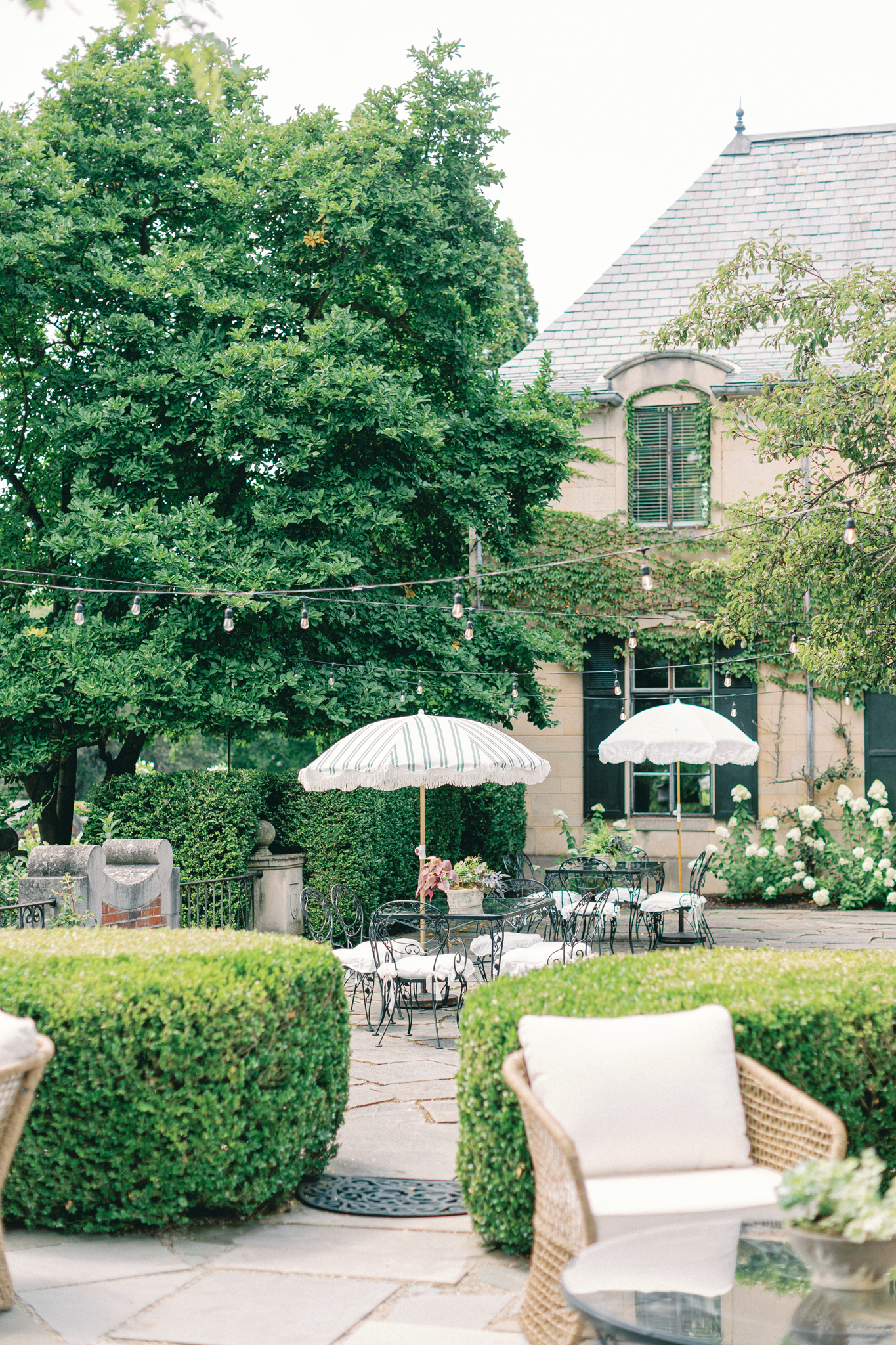 garden patio with fringed umbrellas wicker lounge chairs and string lights at Greencrest Manor Michigan wedding