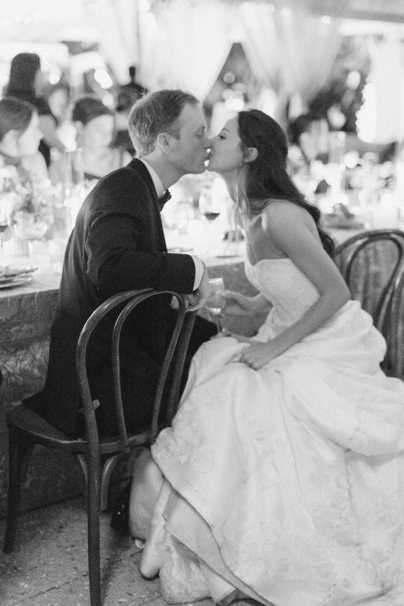 Black and white photo of a bride and groom kissing at their reception table, by a Michigan wedding photographer