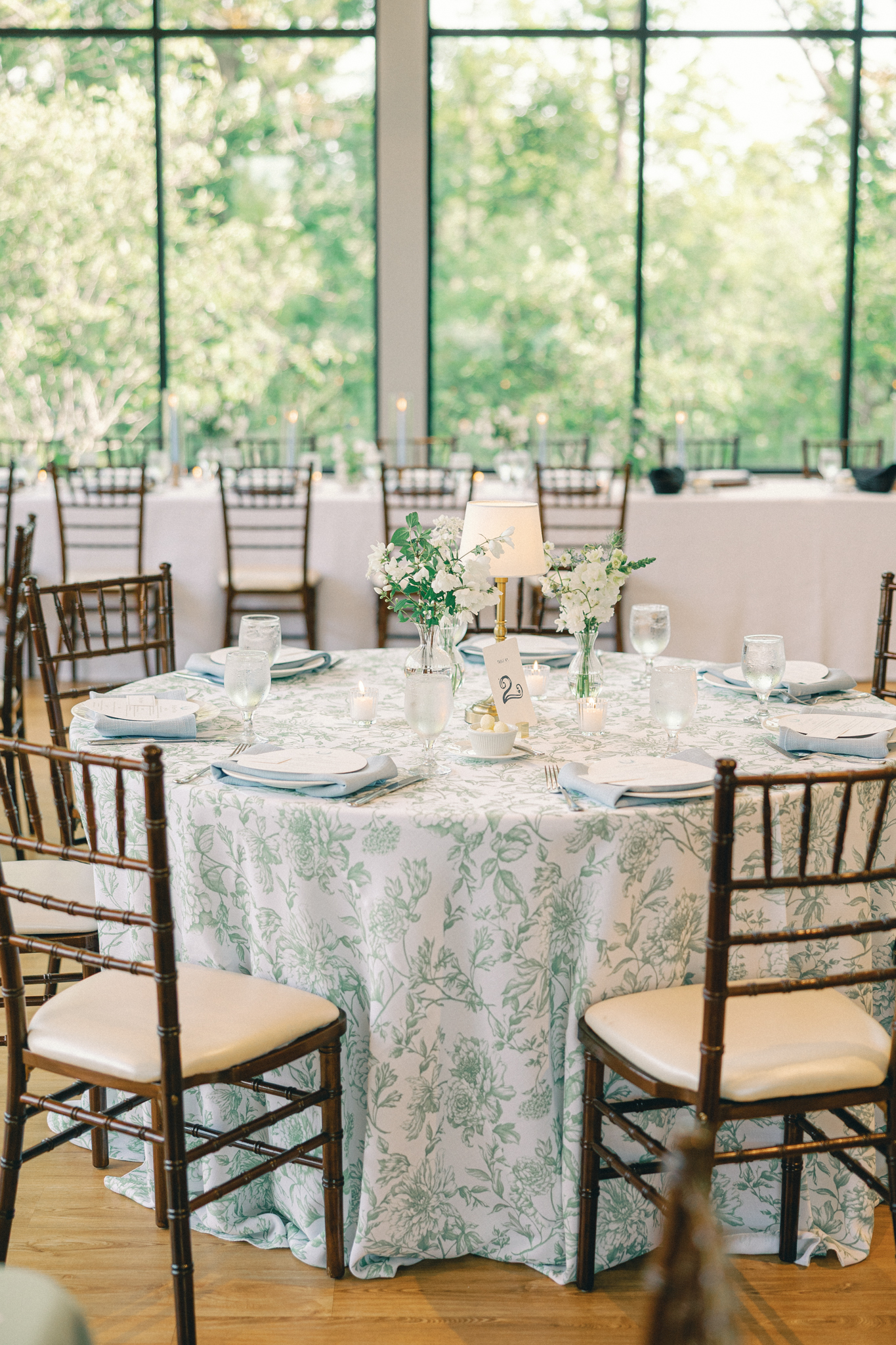 Reception table with a green floral tablecloth, pale blue napkins, and white flowers in summer Michigan wedding colors