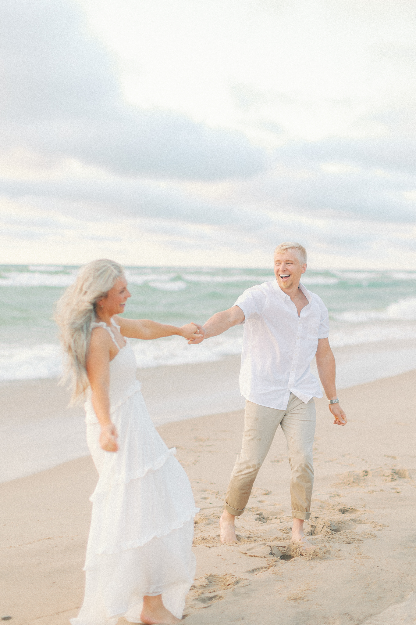 Amber and Adam hold hands at the water's edge at Warren Dunes during their Michigan engagement photos