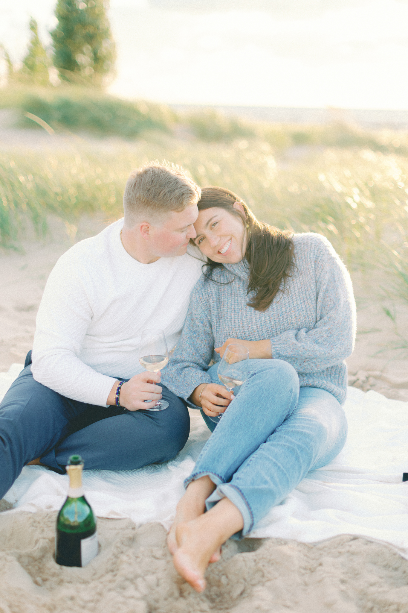Taylor and Joe share a toast on a picnic blanket in the dune grass, a relaxed take on Michigan engagement photography