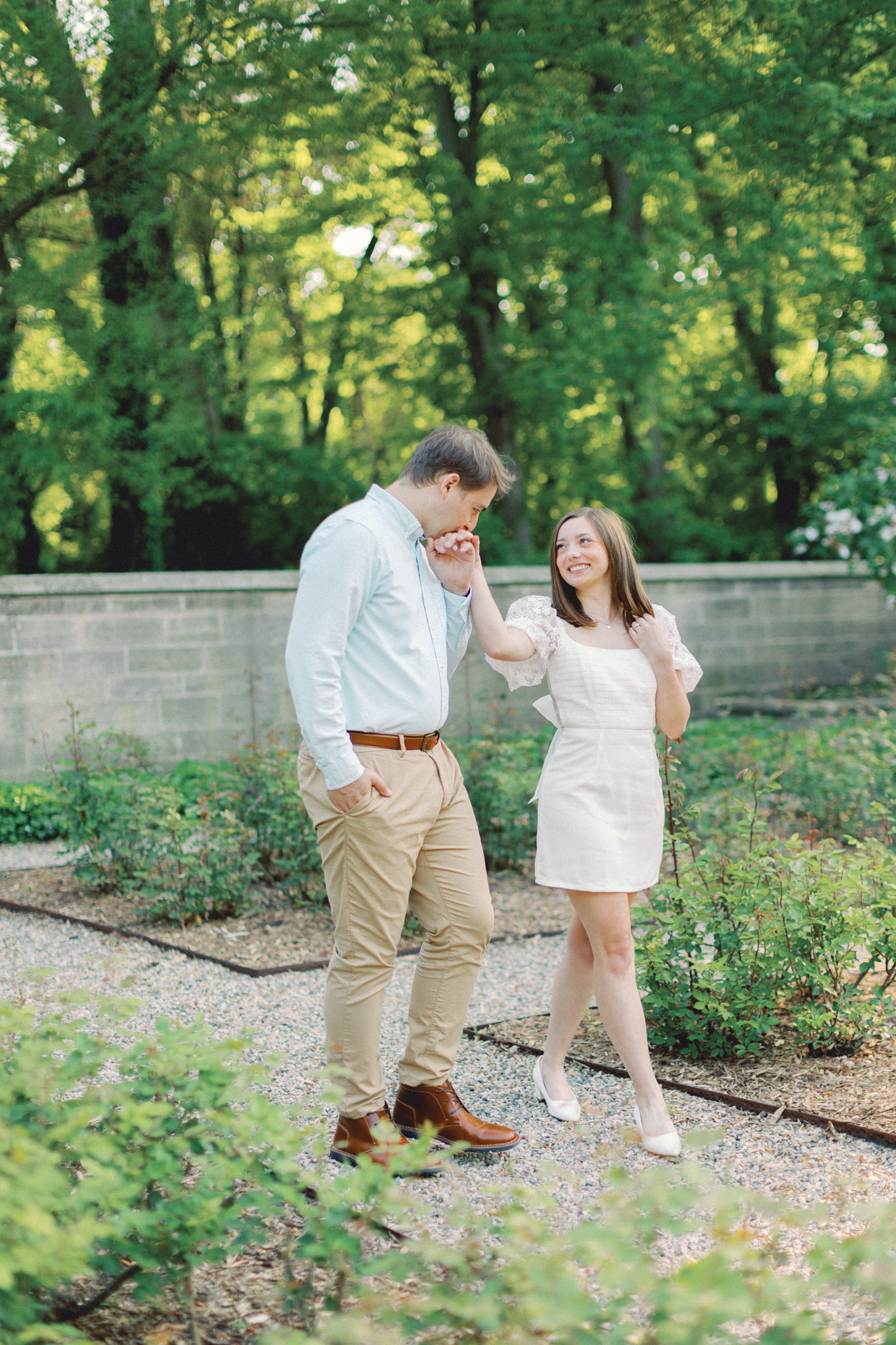 Cameron and Justin share a kiss on the hand in the walled garden at the Ford House, one of the best Michigan engagement photo locations near Detroit