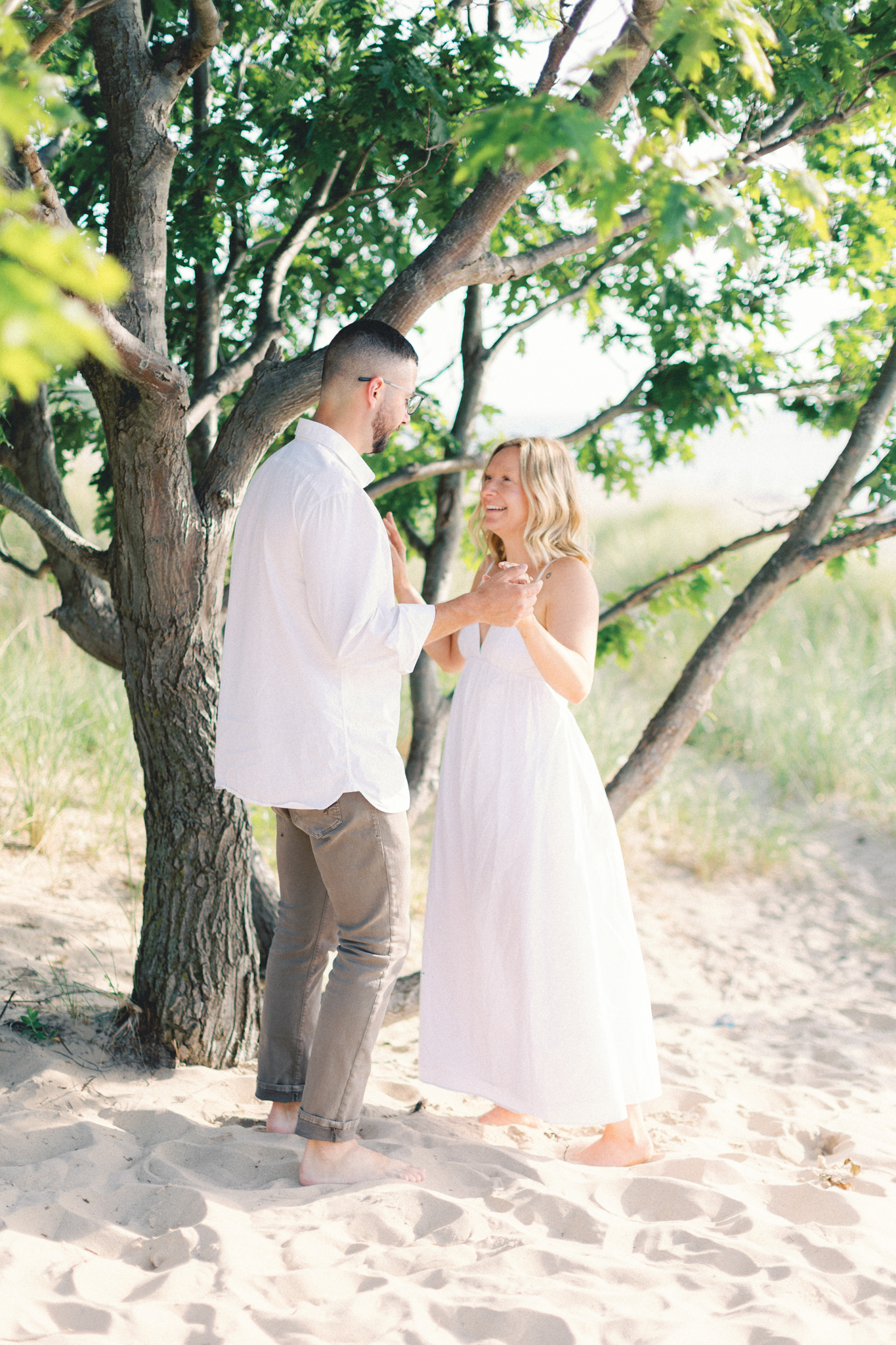 Couple holding hands under a tree on the sand during their Lake Michigan engagement photos